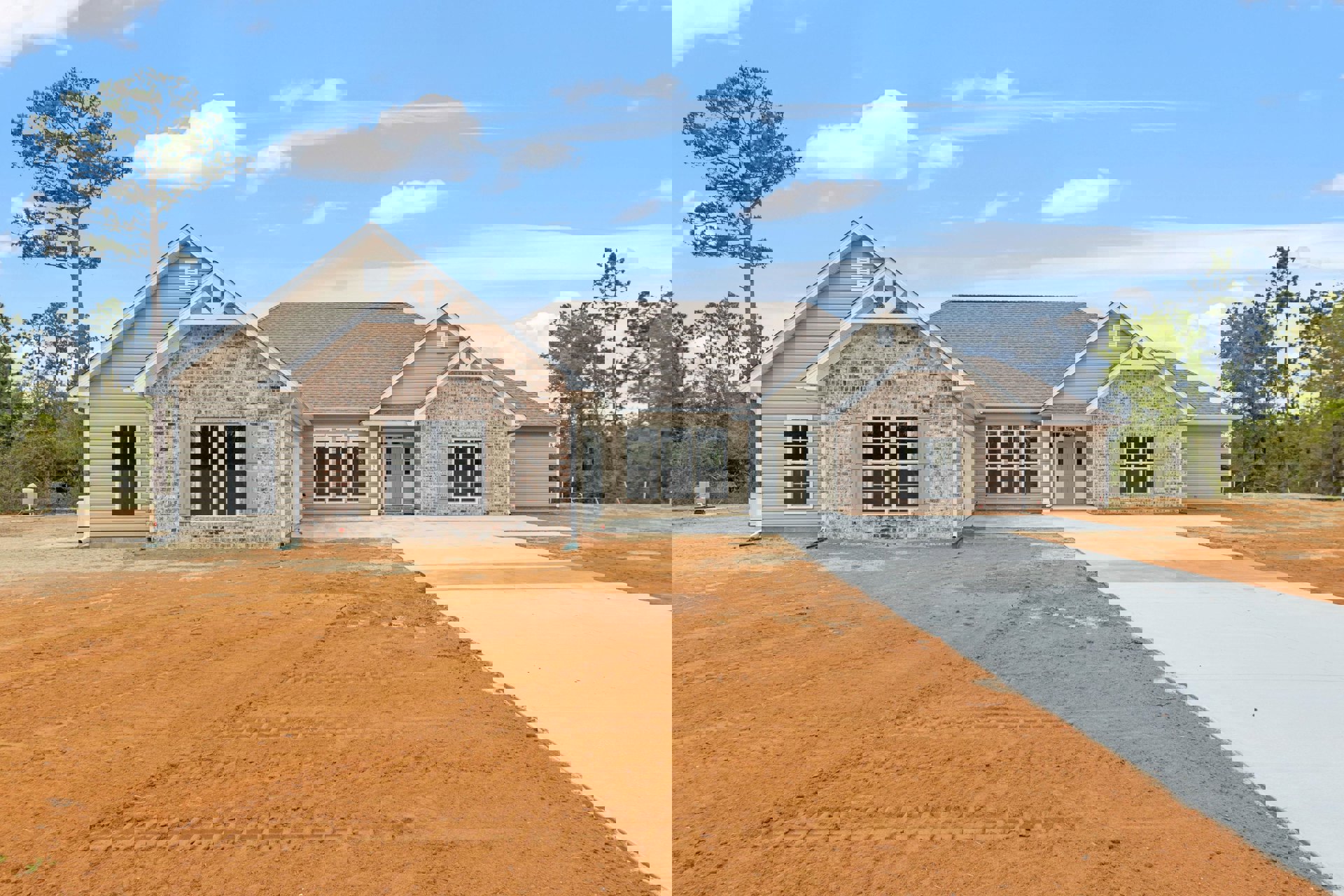 Modern two-story home with white siding, attached garage, concrete driveway with tire tracks, large front windows with white frames, front door, mature trees, and landscaped dirt