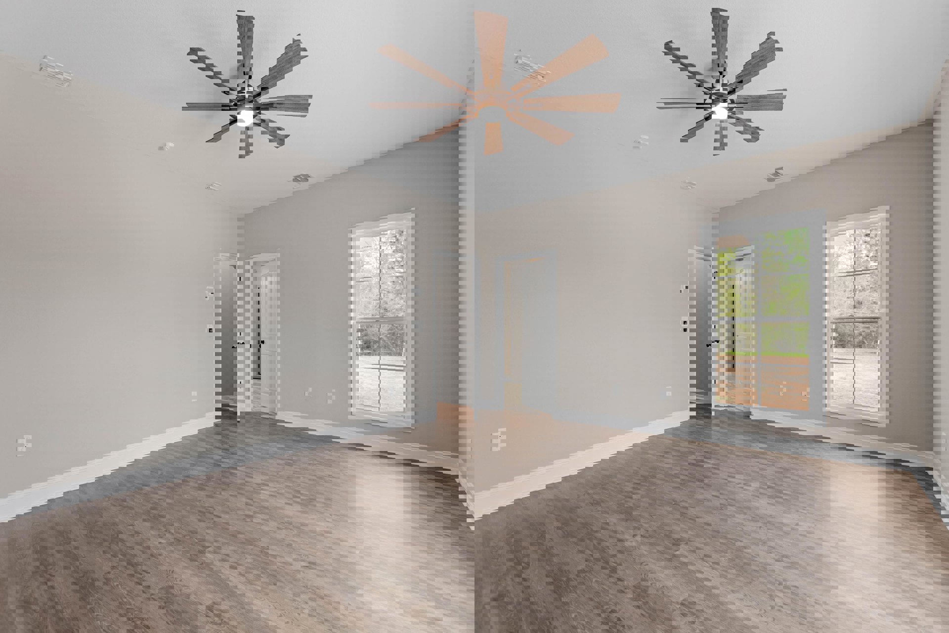 Ceiling fan with light fixture, wood flooring, white walls, white door with black knobs, window showing trees outside, white ceiling with air vent