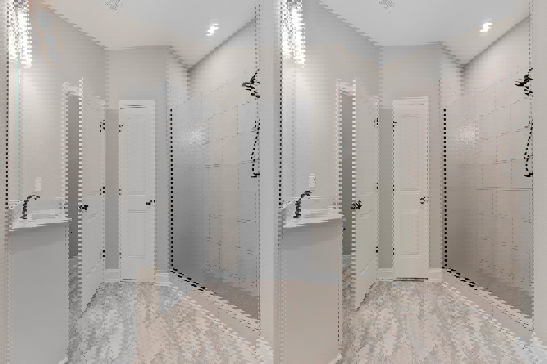 Bathroom with glass shower enclosure, black shower head, white countertop, white cabinetry, and white door with black hardware.