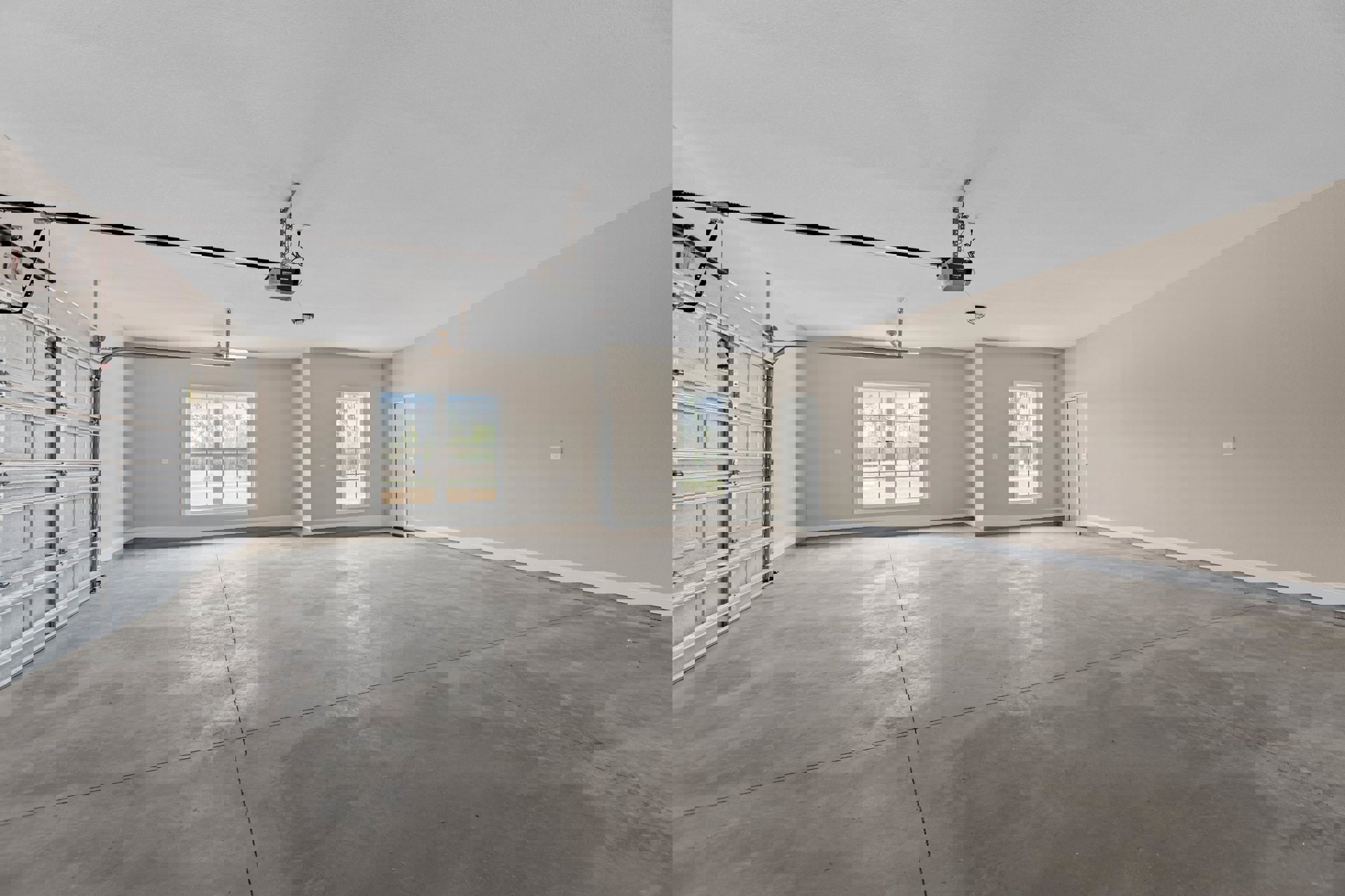 Spacious garage with polished concrete floor, white plaster walls, large window overlooking trees, white door with black handle, metal-framed garage door, ceiling-mounted