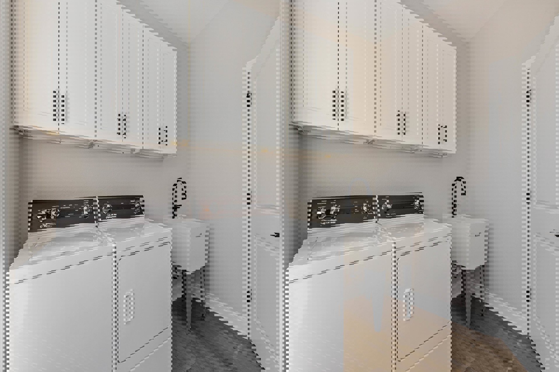 Laundry room with white shaker cabinets, front-loading washer and dryer, white countertop, black lever faucet, and tile backsplash