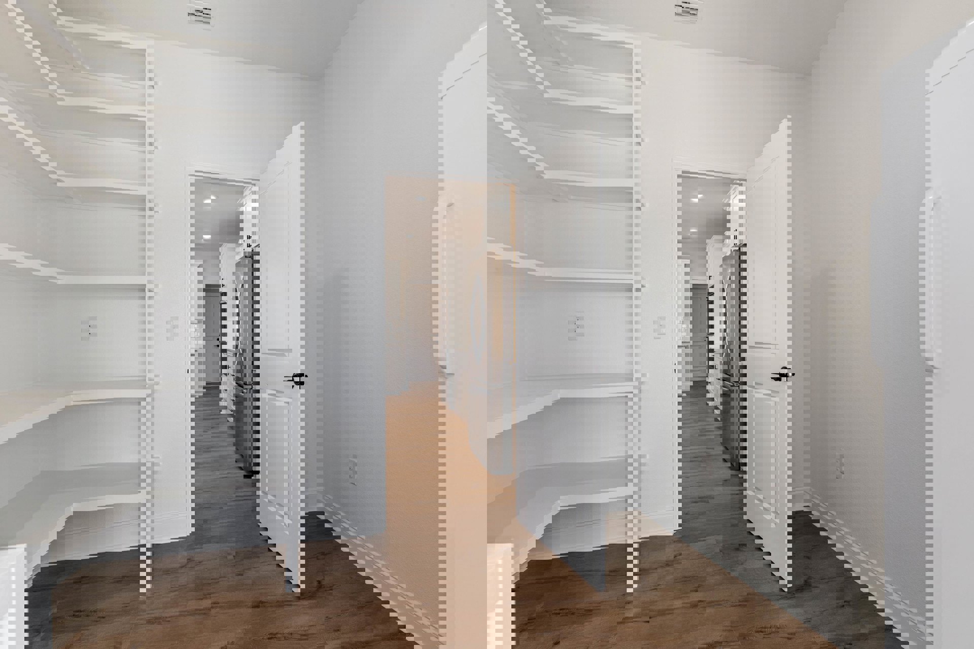 White door with black handle opening to kitchen featuring stainless steel refrigerator, white shelves, wood flooring, and white walls.
