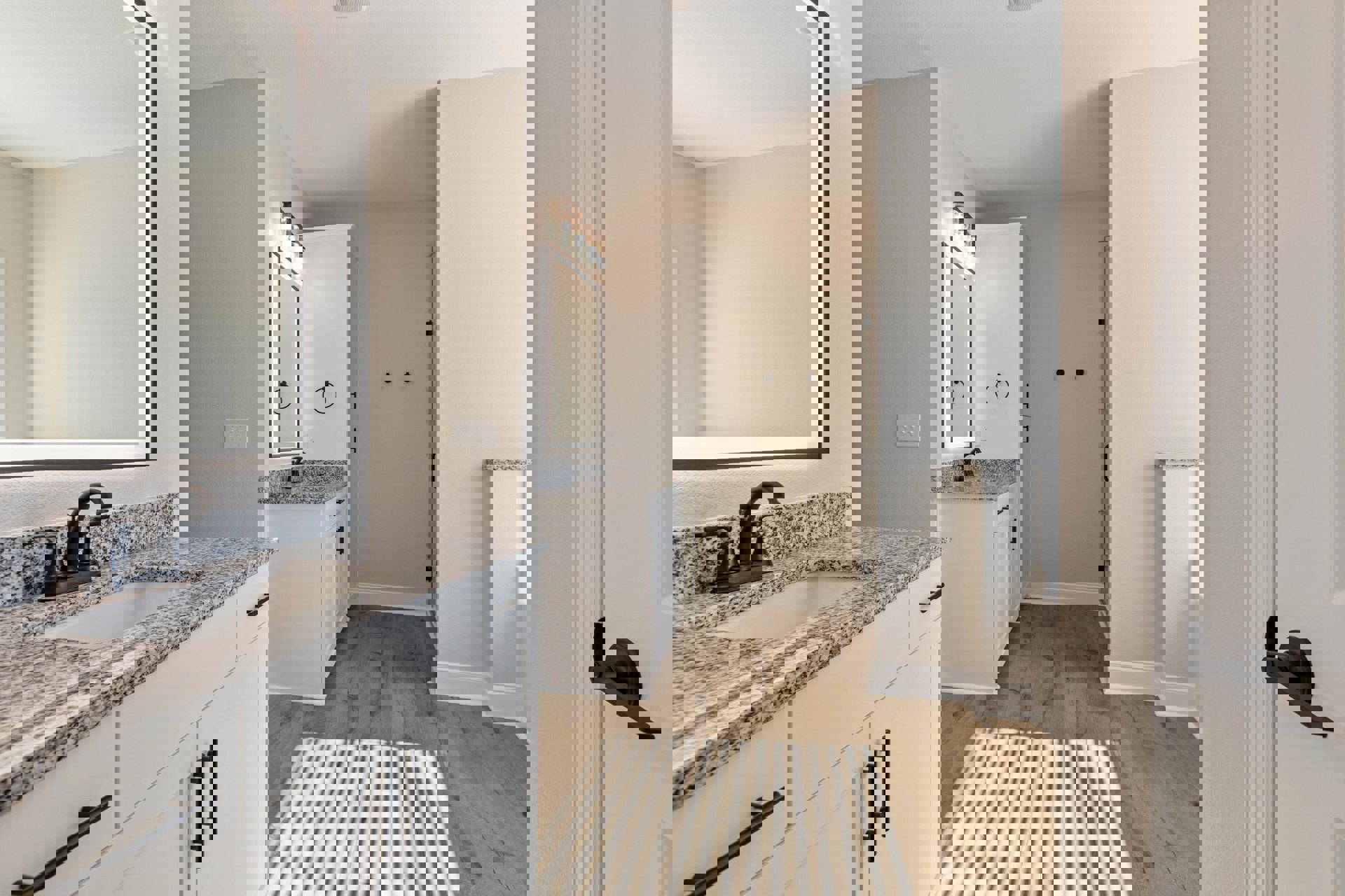 Bathroom featuring marble countertops, wood flooring, white cabinetry, undermount sink with chrome faucet, and white walls with a door frame and black hardware