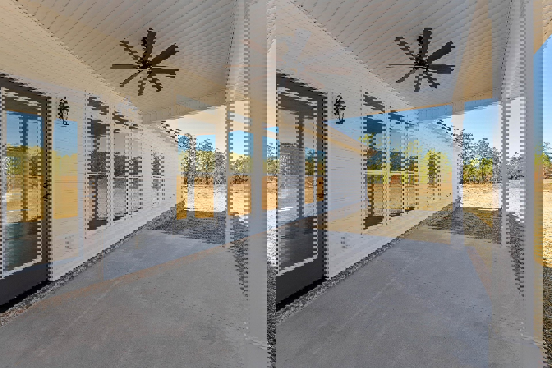 White exterior home with covered porch, ceiling fan and light fixture, glass door, concrete driveway, and windows under blue sky.