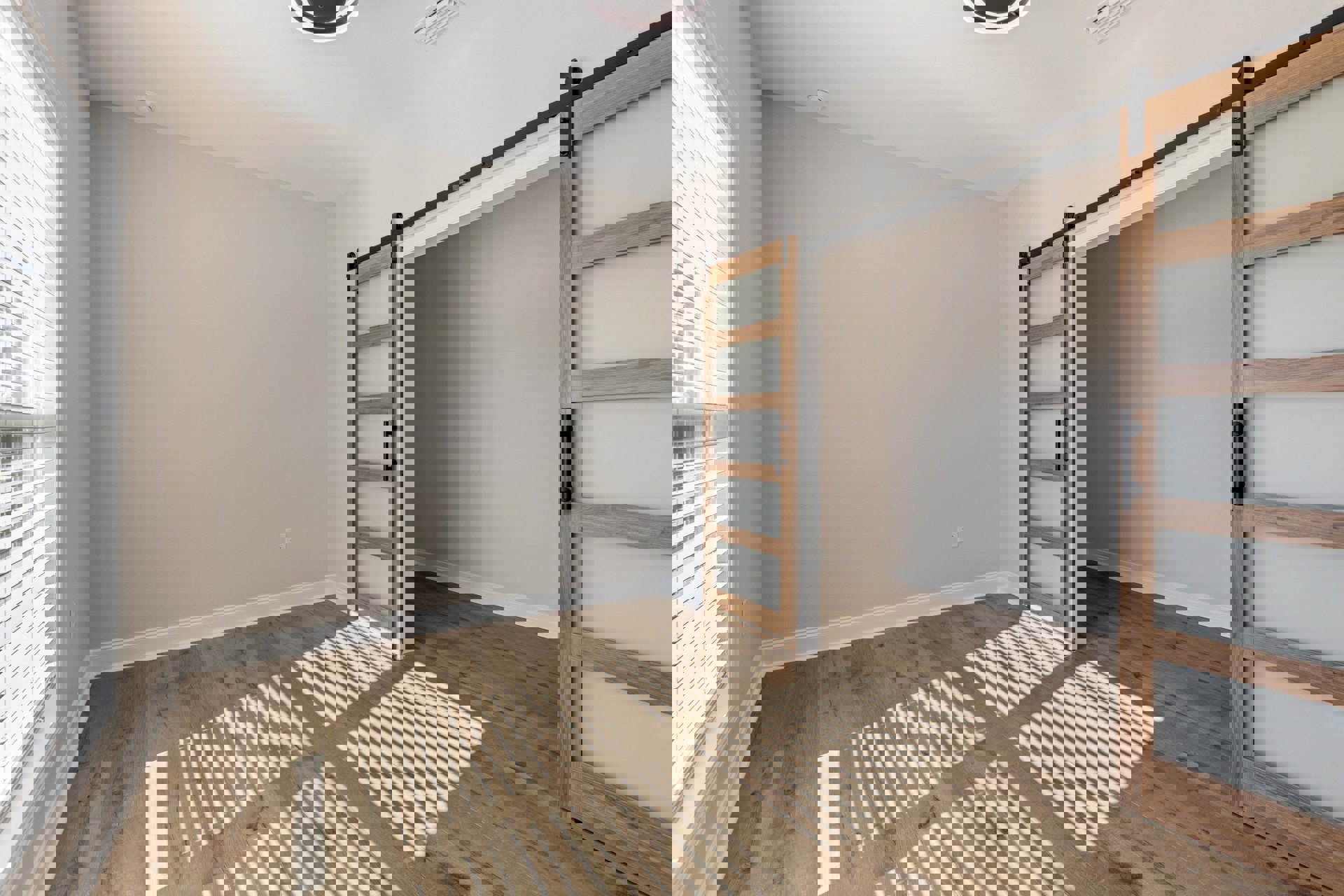 Sliding glass door with black handle, wooden floor, white walls, and window with horizontal blinds