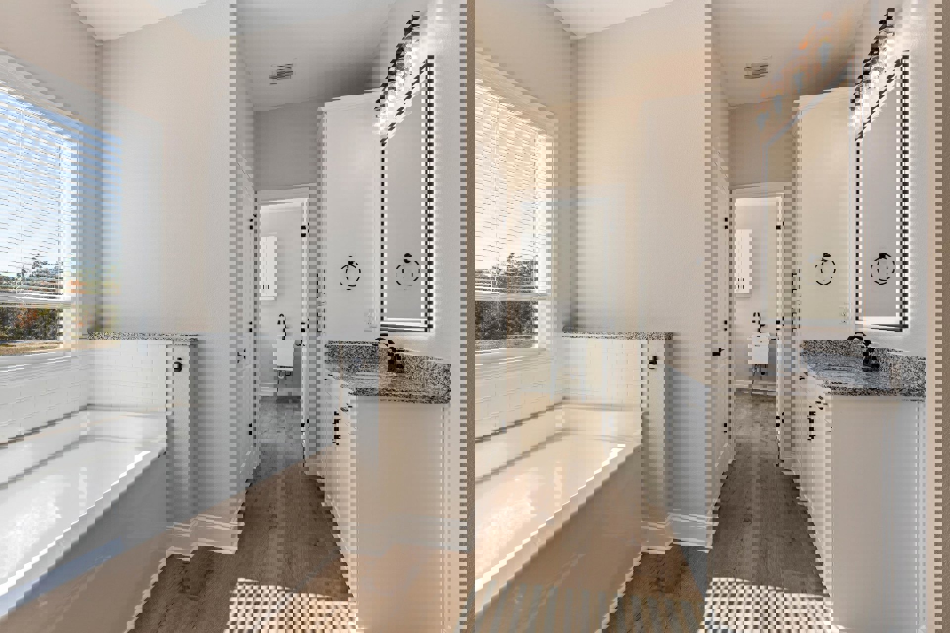 Freestanding white bathtub beside a modern sink, black towel holder mounted on white tiled wall, window with white blinds, partial view of door and countertop with round black