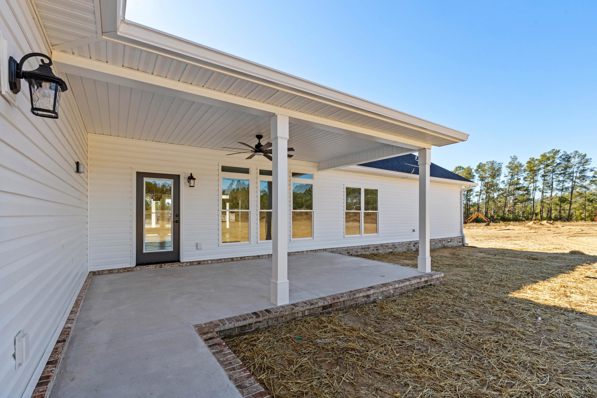 White siding house with covered porch, ceiling fan, glass door, white-framed windows, and surrounding trees