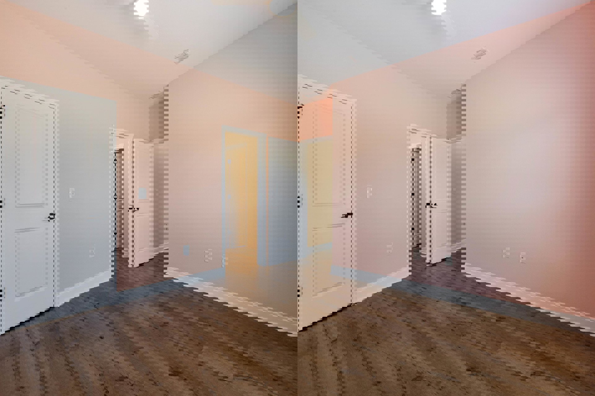 Pink walls, wood laminate flooring, white door with black handle, ceiling fan, air vent, plaster finishes