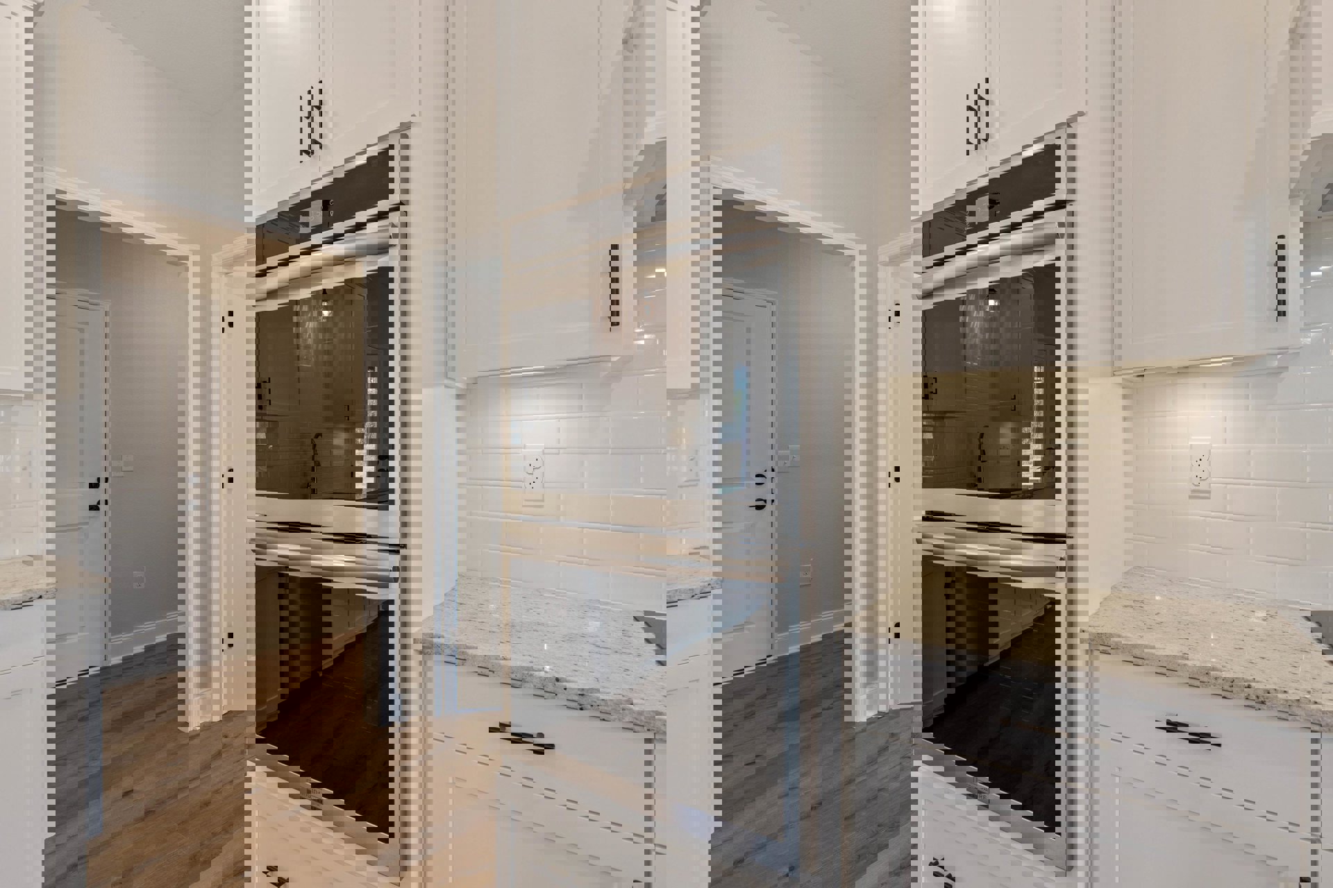 White kitchen cabinets, stainless steel ovens with black glass doors, glass door refrigerator, white countertop, white door with black handle