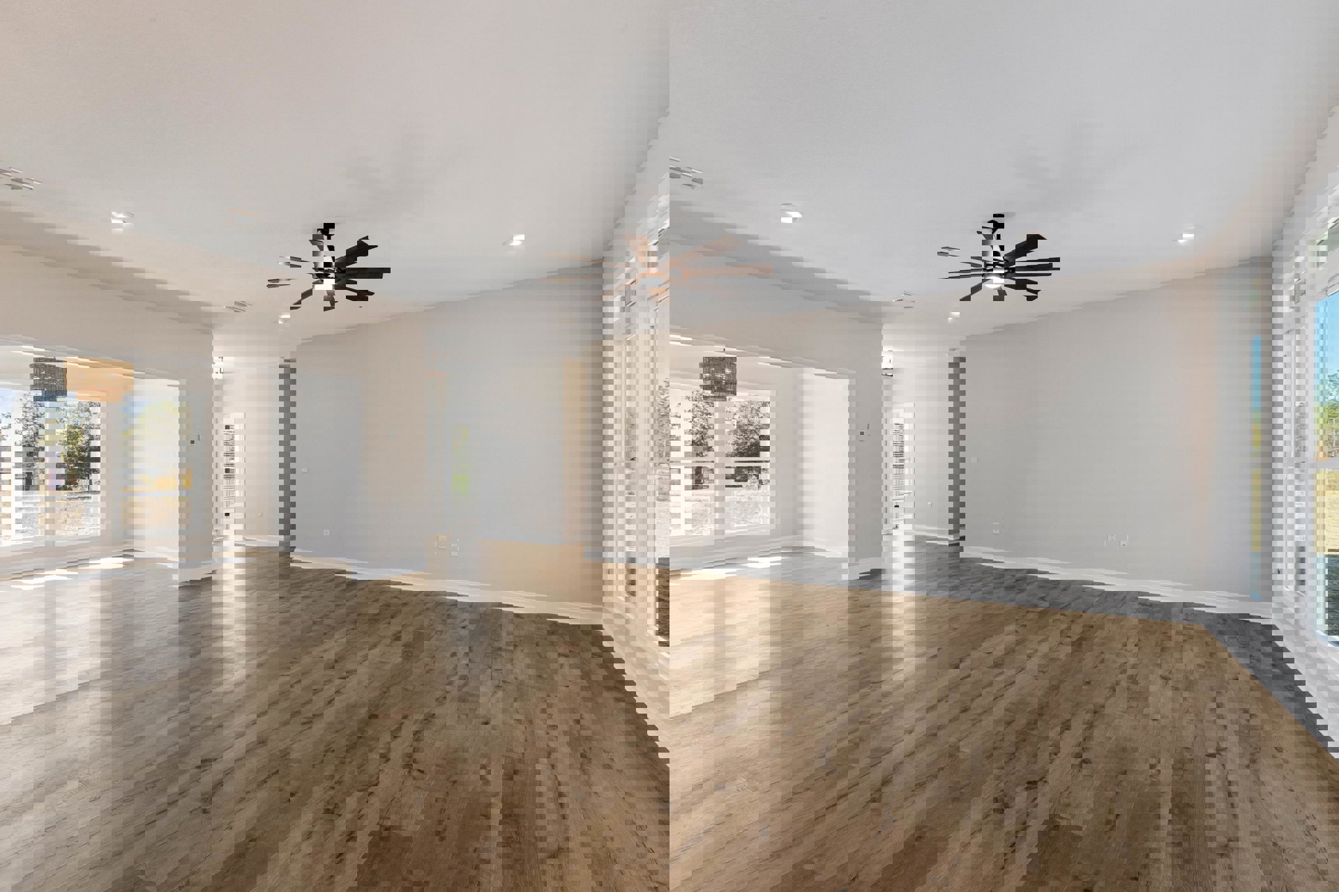 Spacious room featuring hardwood flooring, white walls, and a ceiling fan with integrated light fixture