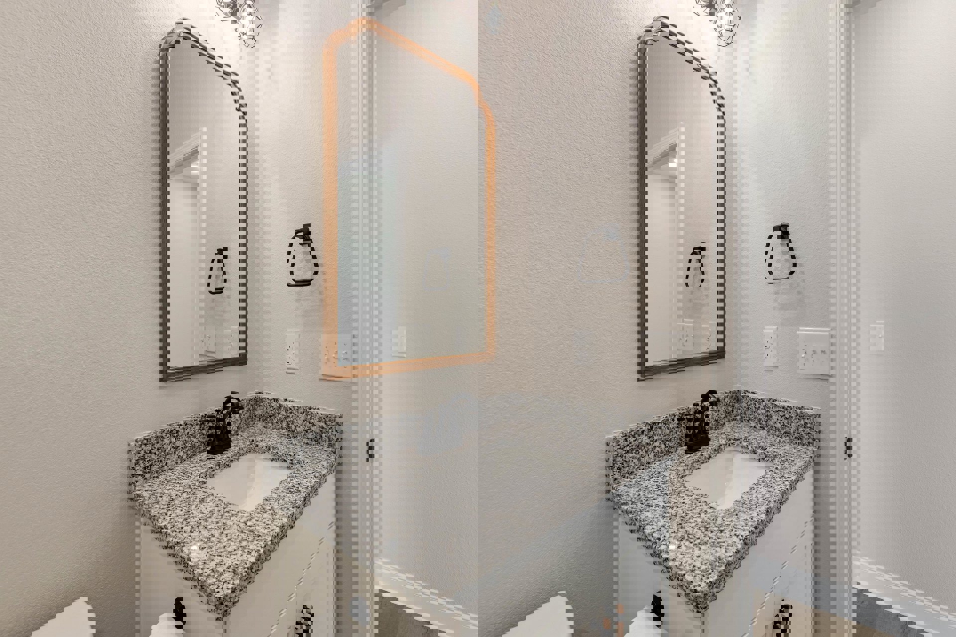 Marble countertop vanity with rectangular sink, black faucet, wall-mounted mirror, white tile backsplash, and row of light switches on adjacent wall