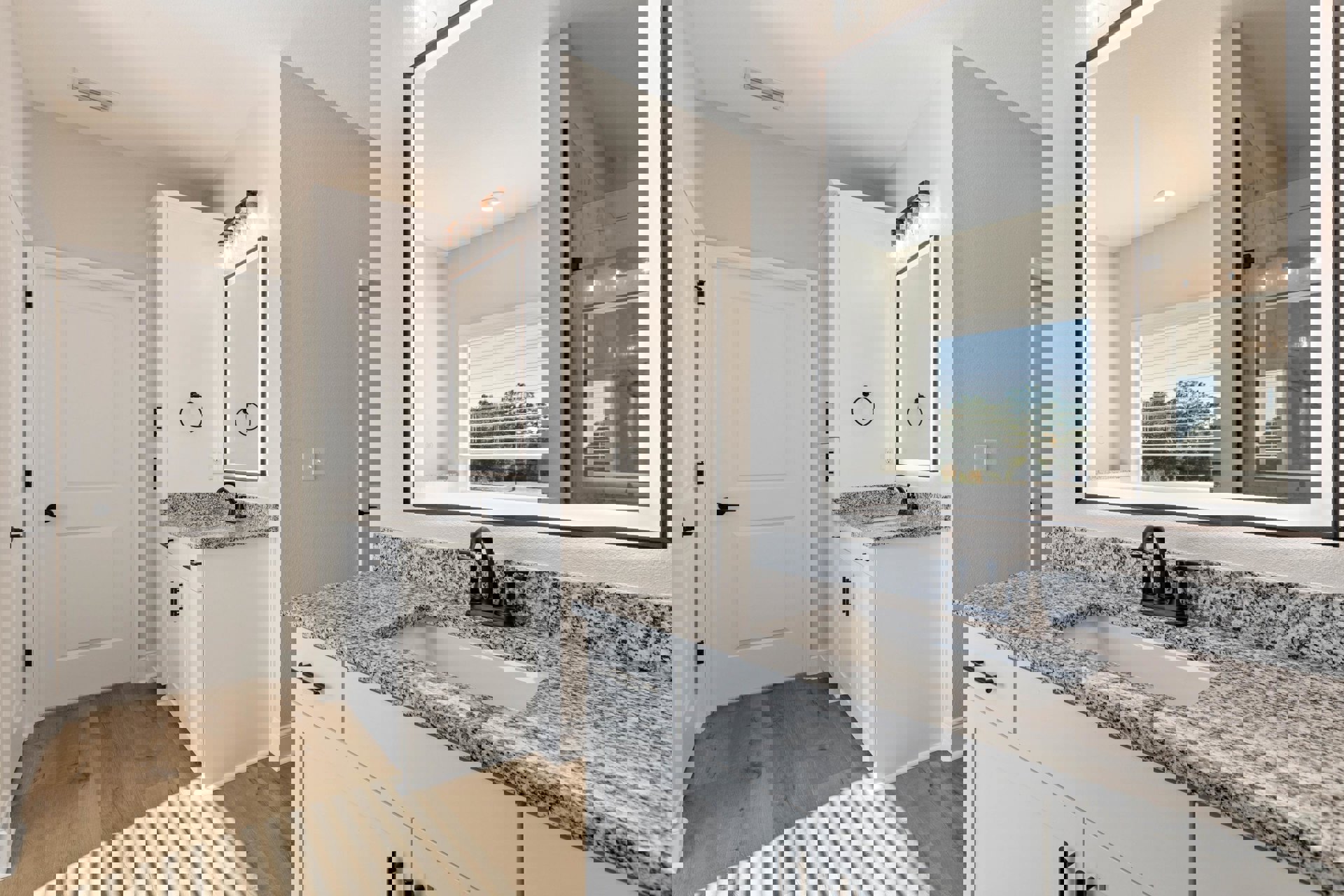 Bathroom with marble countertop, rectangular mirror above sink, black faucet and towel holder, white walls and door with black handle, window with white blinds