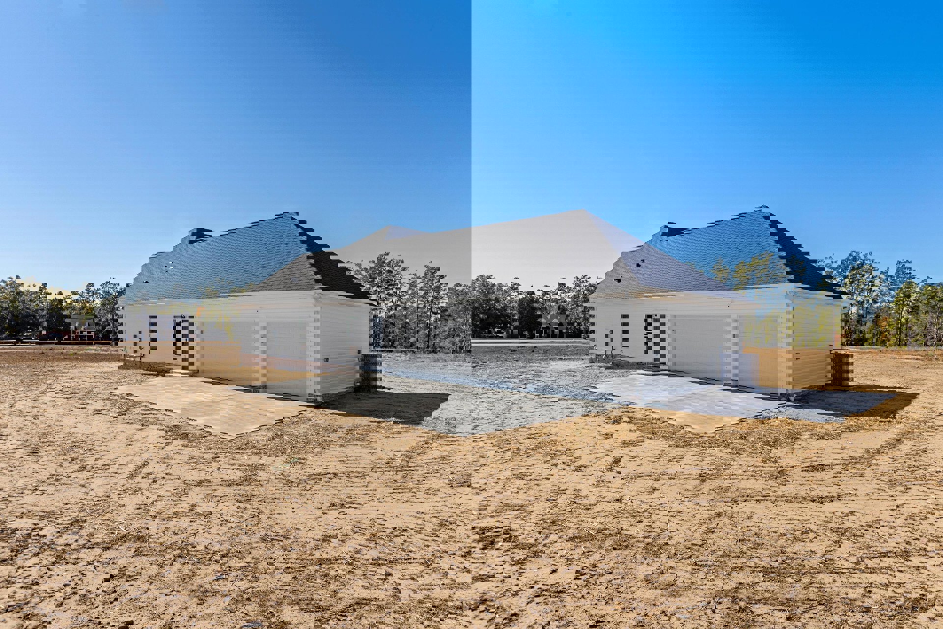 Two-story house with gray siding, attached two-car garage, unfinished dirt driveway, black mailbox, and sparse landscaping under a clear sky
