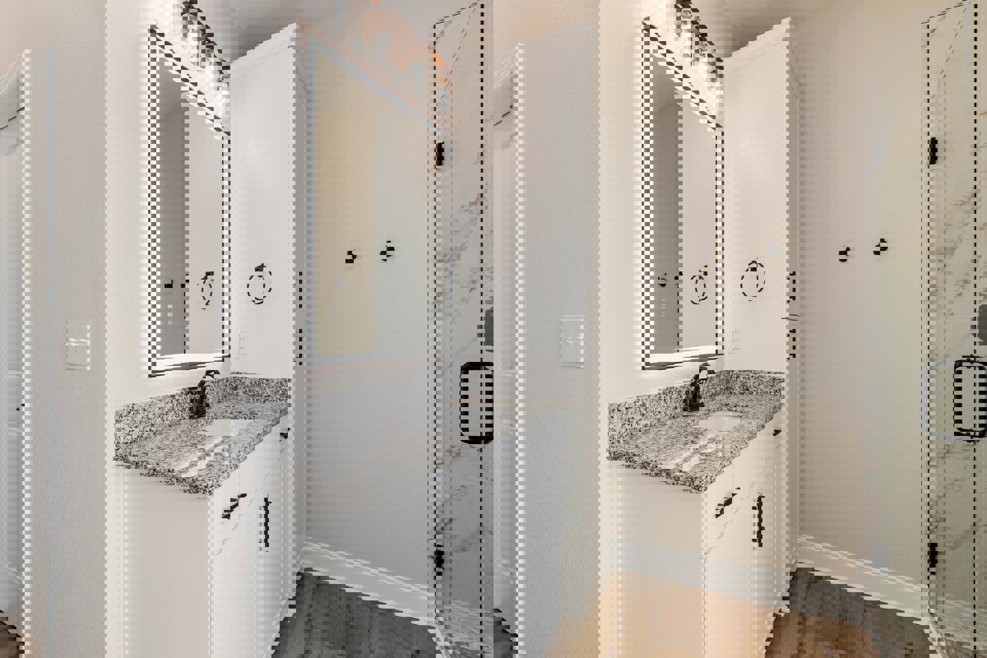 White bathroom with rectangular mirror above a modern sink, black towel holder mounted on wall, glass shower door with black handle, white tile surfaces, and minimal cabinetry.