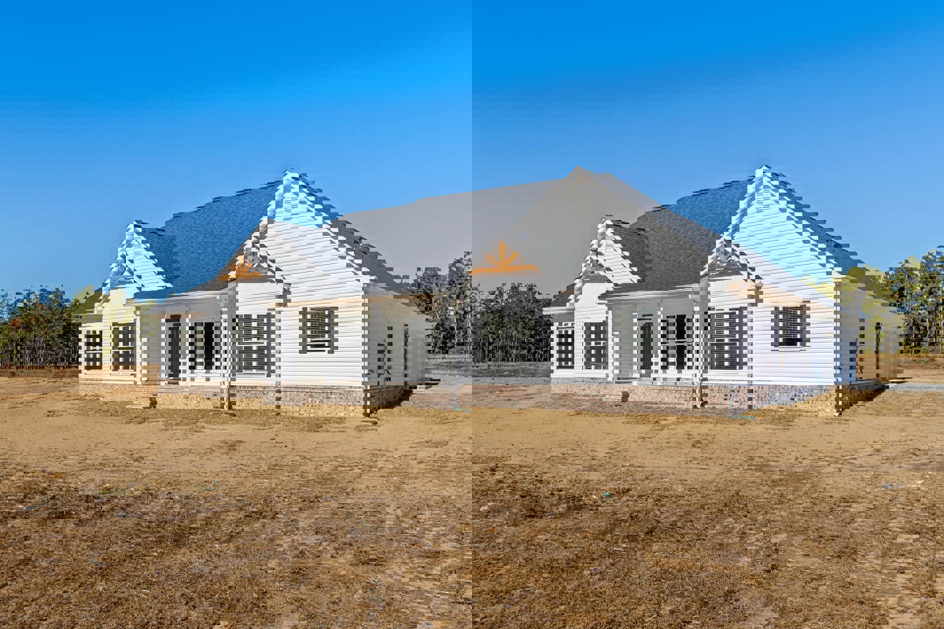 White house with black roof set on a dirt field, surrounded by scattered trees, large windows visible on the exterior