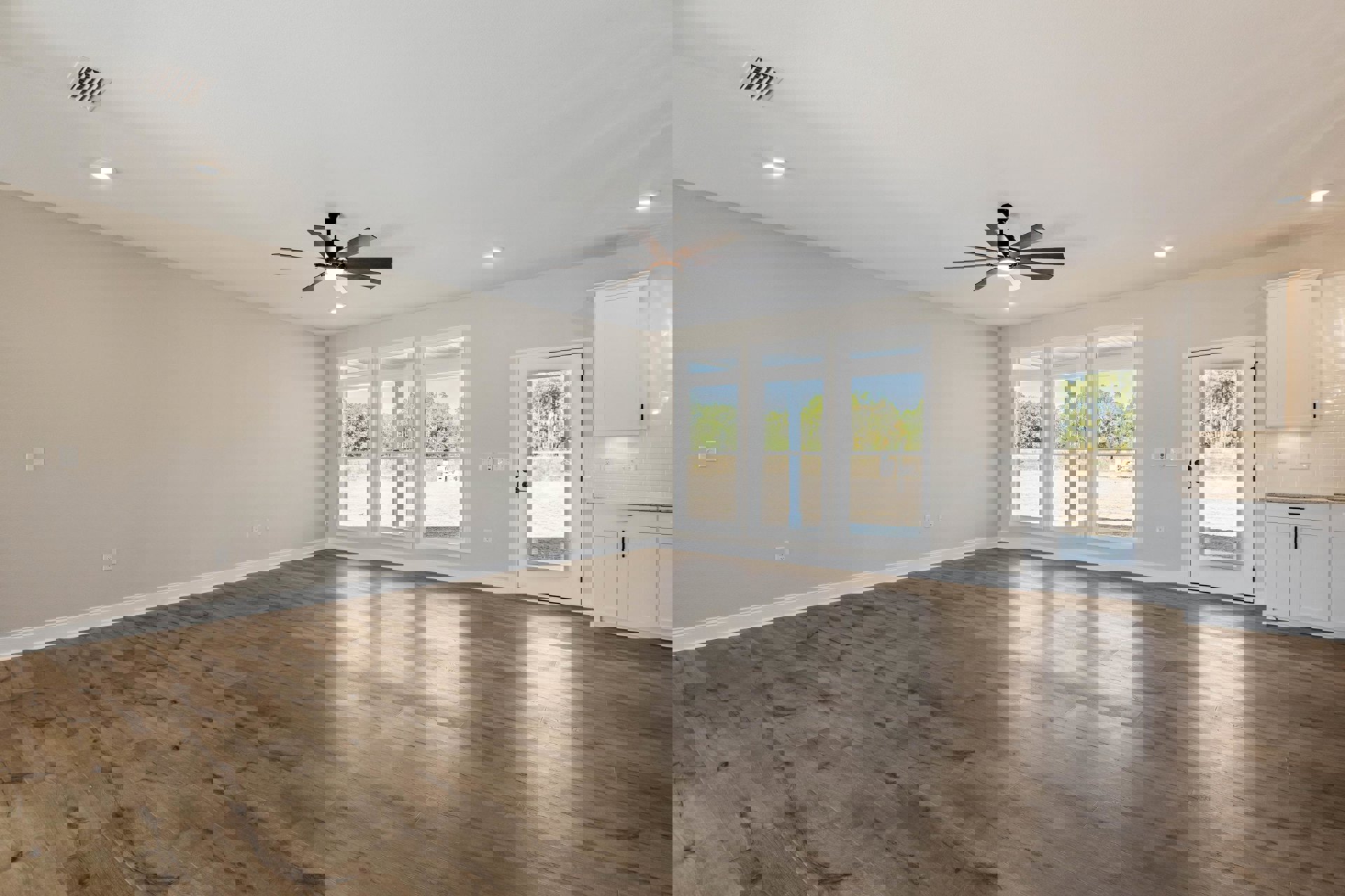 Ceiling fan with light fixture, wood laminate flooring, white plaster walls, glass door, large windows overlooking trees