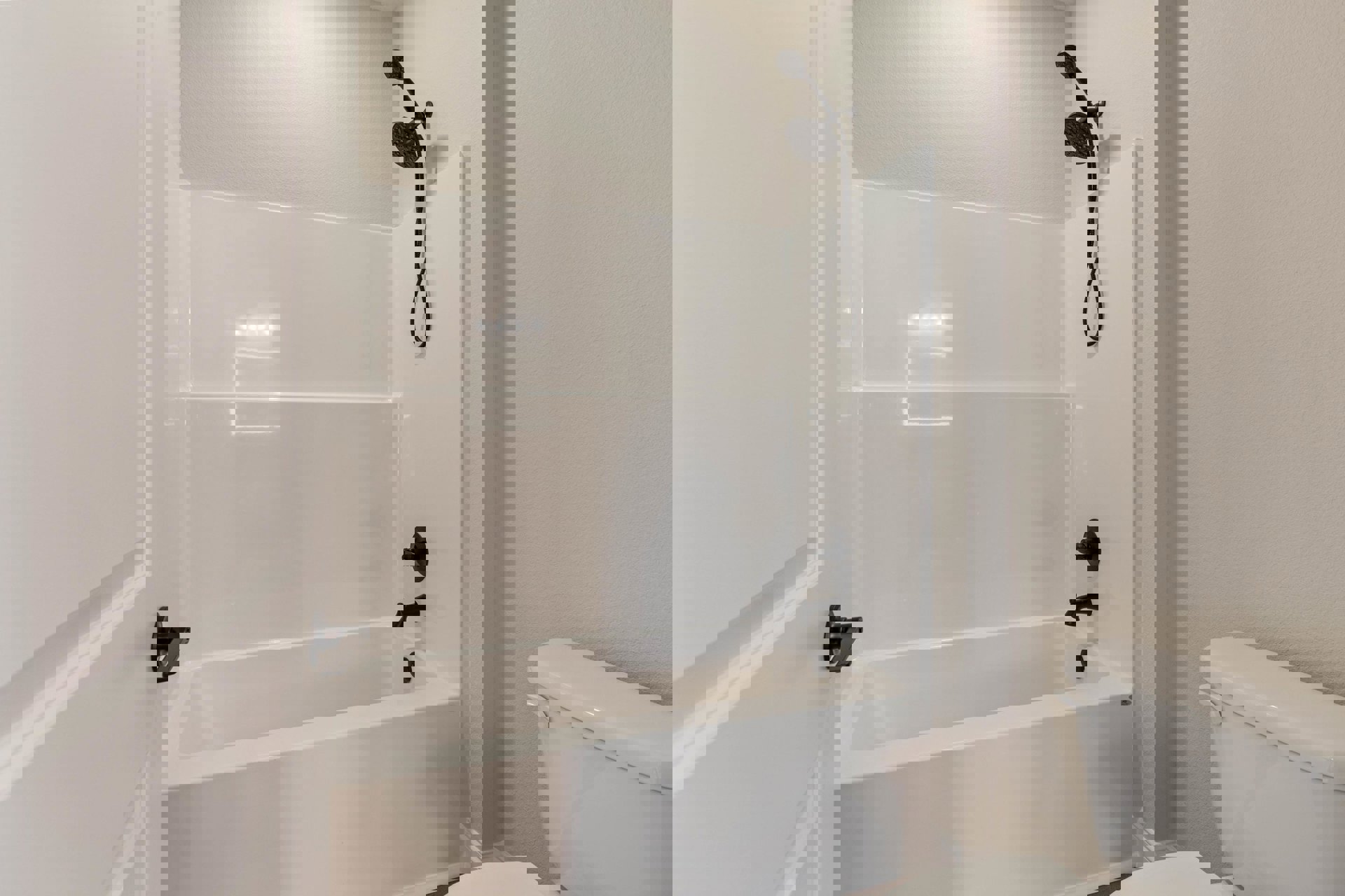 White bathtub with matte black fixtures beside a white toilet, light gray tile walls, handheld shower head, and chrome door handle visible in foreground