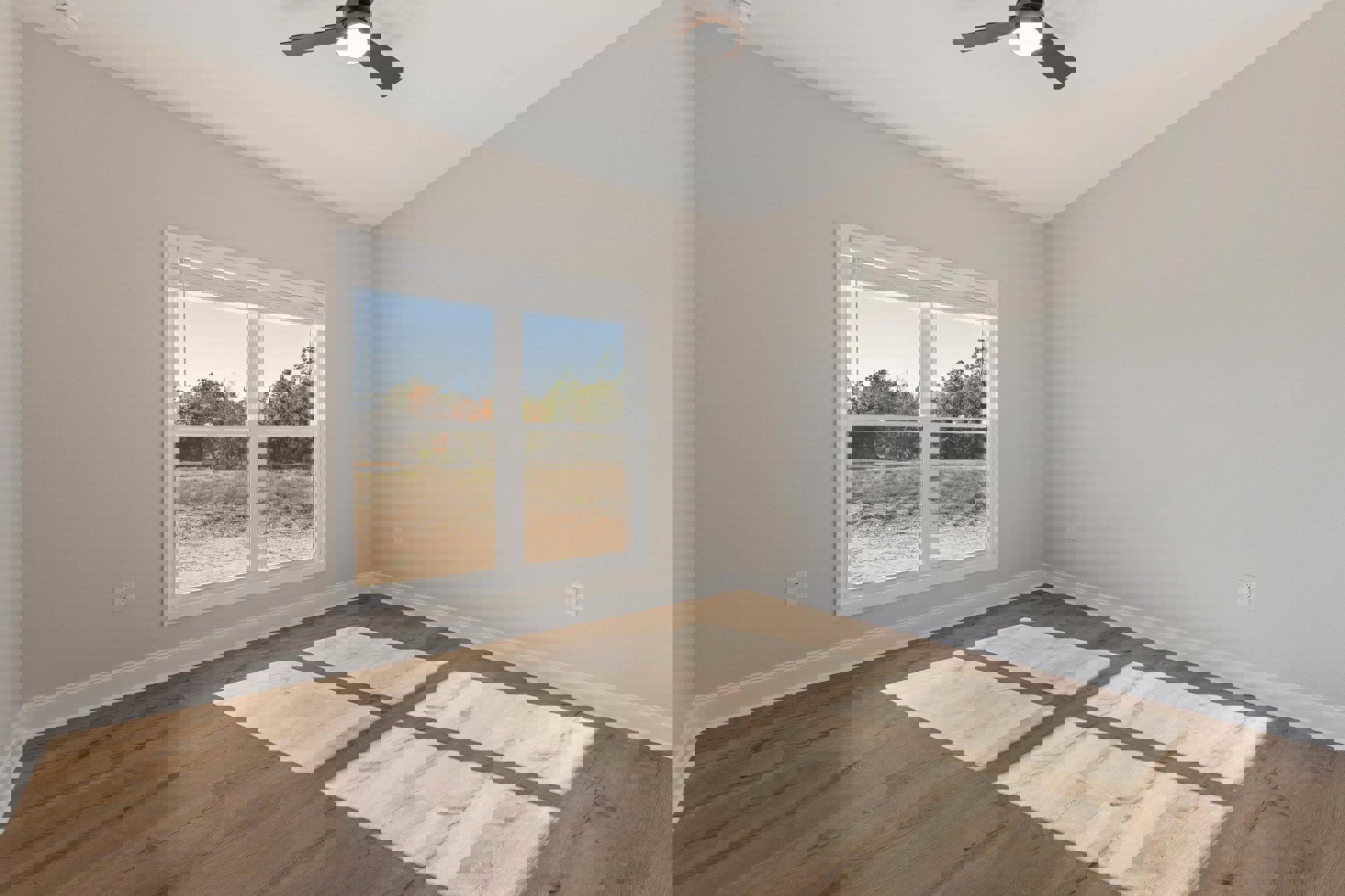 Sunlit room with wood laminate flooring, plaster walls, large window overlooking trees, and ceiling fan with light fixture