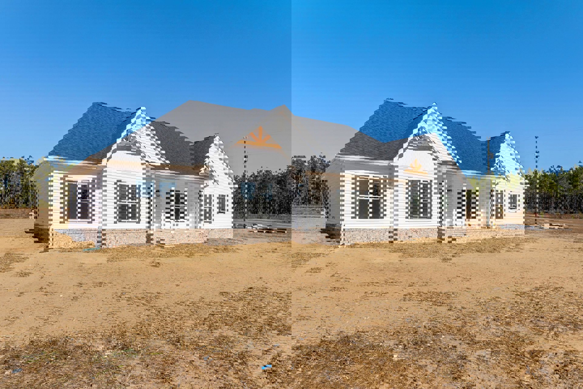 White house with black roof, dirt yard in foreground, large windows with blinds, minimal landscaping, clear sky above