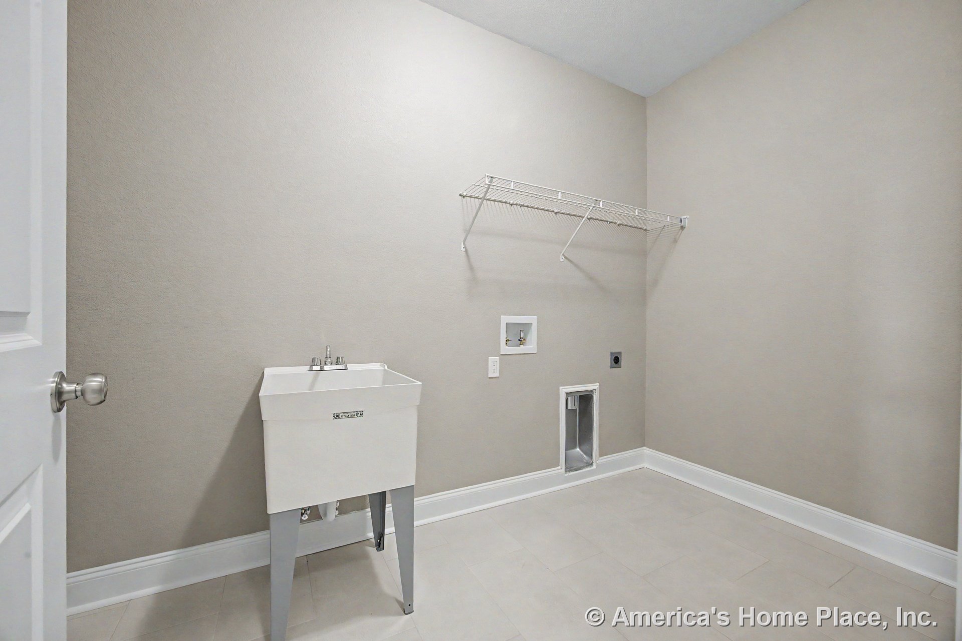 Laundry room with utility sink and faucet, tile flooring, wall-mounted wire shelf, washer and dryer hookups, white baseboards, and neutral painted walls.