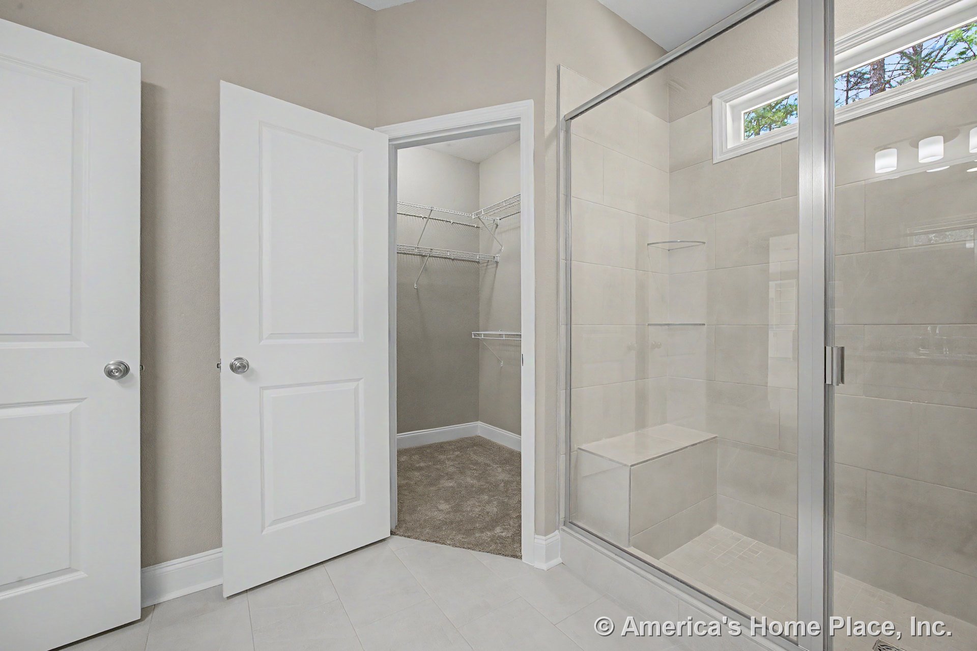Frameless glass walk-in shower with built-in bench, rectangular tile flooring, white paneled doors, walk-in closet featuring wire shelving, and transom window above shower.