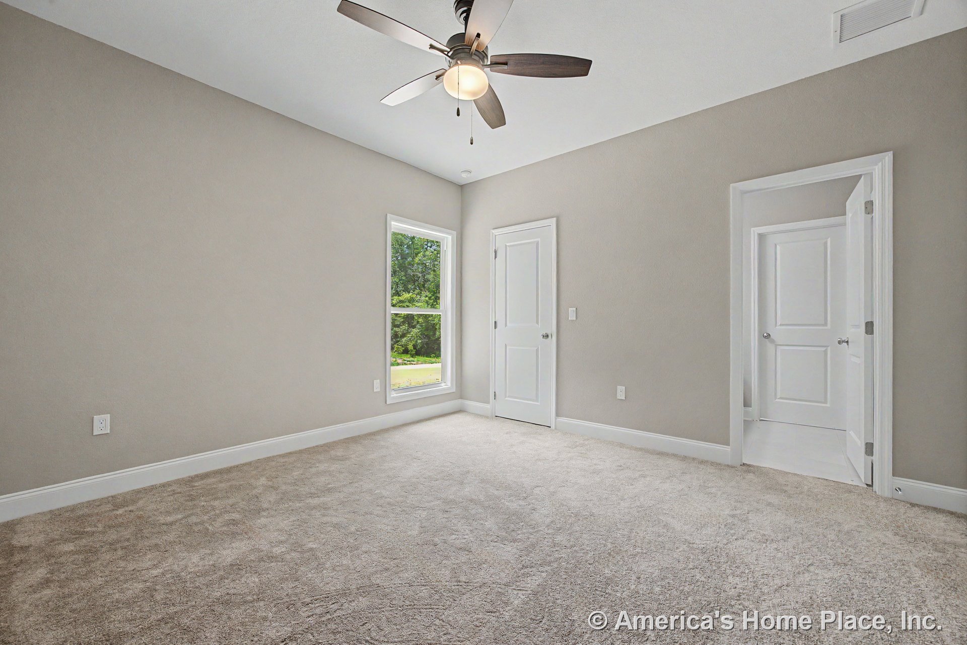 Beige carpet flooring in a bedroom with neutral painted walls, white baseboards, large window with white trim, ceiling fan and light fixture, and two white paneled doors.
