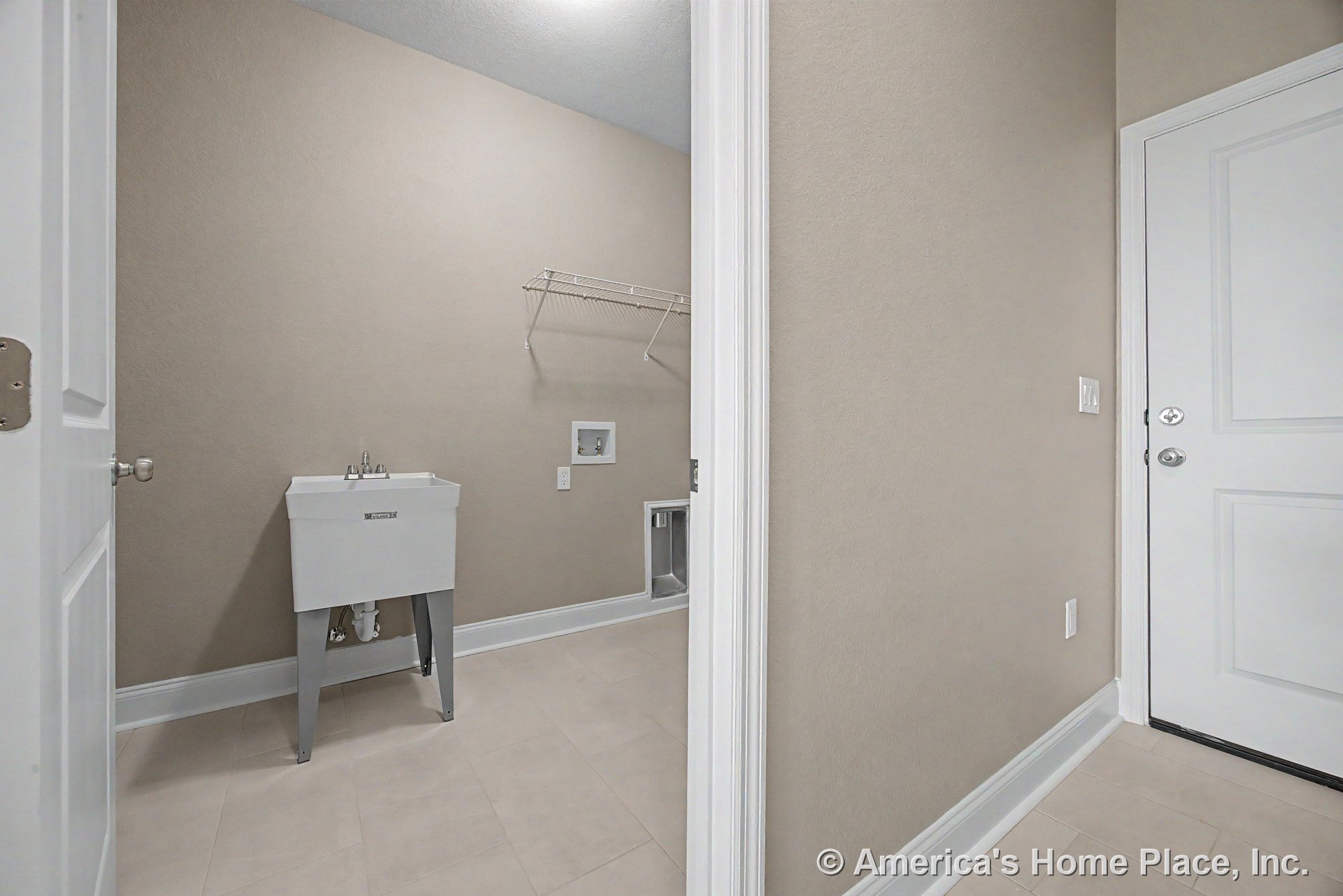 Laundry room with utility sink, beige tile flooring, wire shelving above washer and dryer hookups, white baseboard trim, solid panel door, and built-in ceiling lighting.