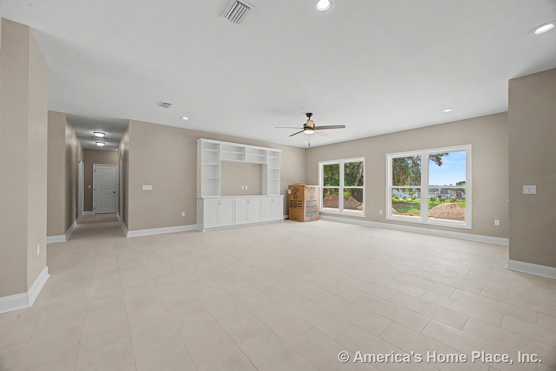 Spacious living room with built-in white entertainment center, three-panel picture windows, ceiling fan with light, recessed ceiling lights, neutral beige walls, rectangular tile