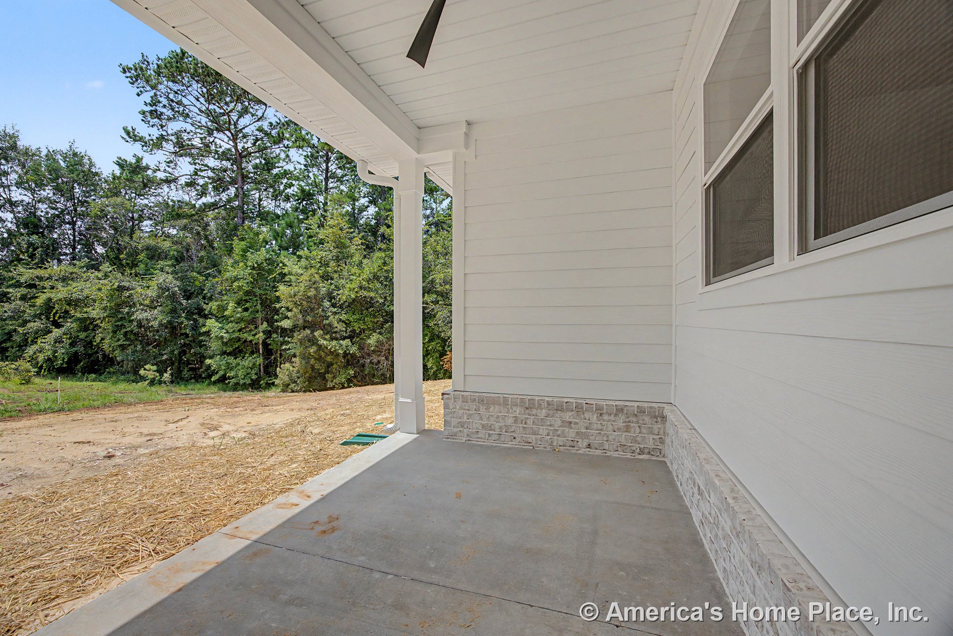 Covered porch with concrete flooring, white horizontal siding, brick trim base, double window, and ceiling fan.