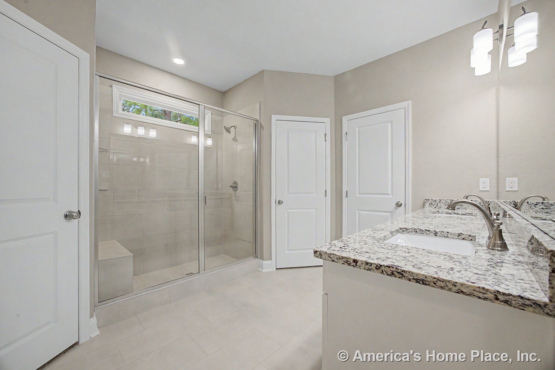 Spacious bathroom with glass-enclosed shower, granite vanity countertop, dual undermount sinks, recessed ceiling lights, modern wall sconces, tile flooring, white cabinetry, and