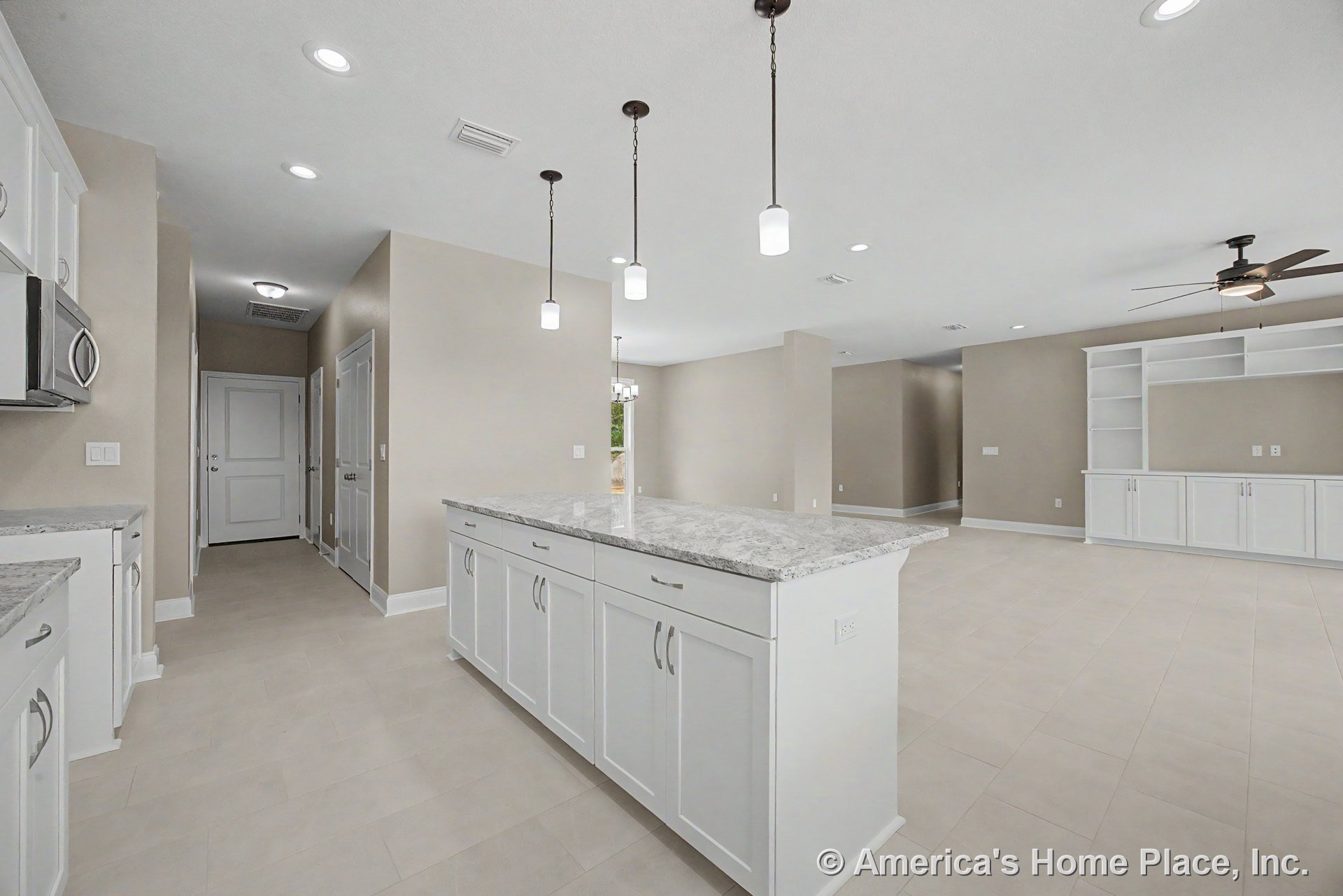 Large kitchen island with white shaker cabinets and granite countertops, pendant lighting above, tile flooring throughout, open to living area with built-in shelving, neutral wall