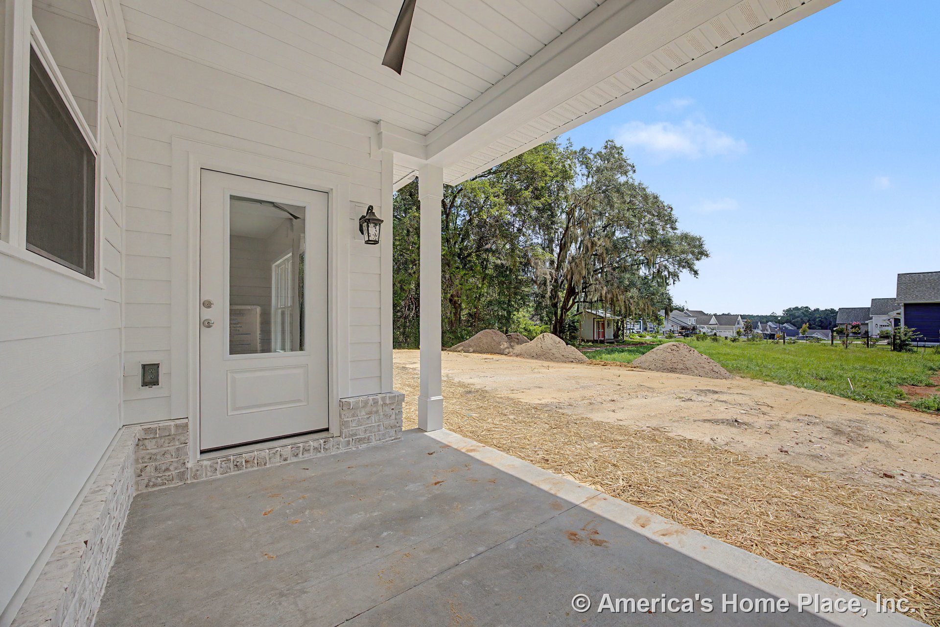 Covered front porch with white horizontal siding, concrete floor, glass exterior door, brick trim base, ceiling fan, wall-mounted lantern light, and adjacent windows.