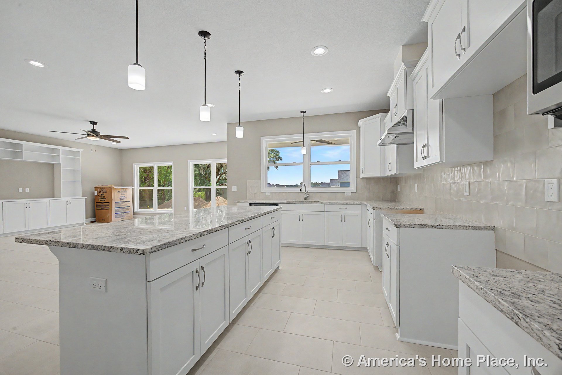 White shaker kitchen cabinets, granite island with pendant ceiling lights, tile backsplash, and tile flooring; open concept layout with large windows and built-in living room