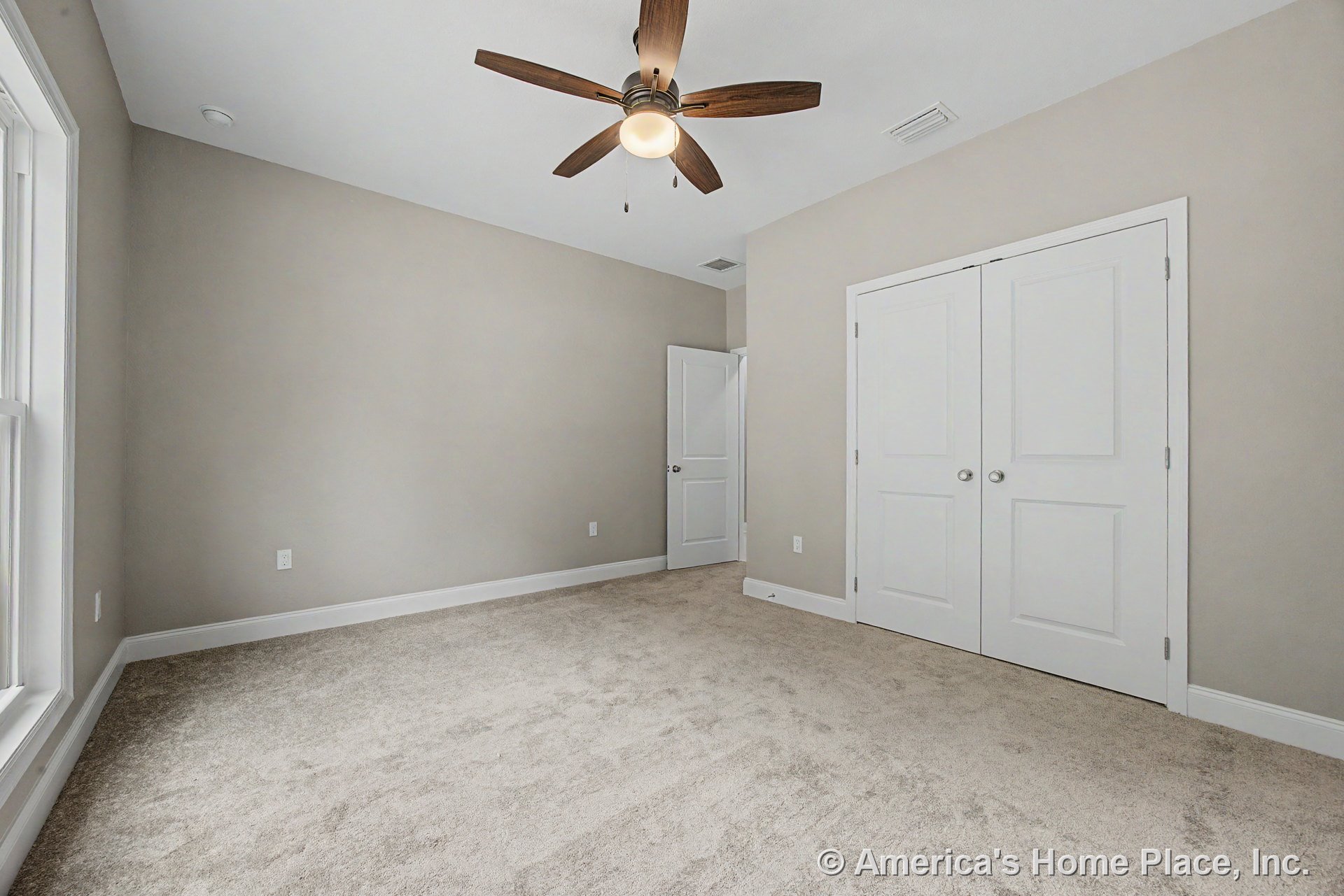 Beige carpet flooring, white double closet doors, ceiling fan with light fixture, large window, neutral wall color, and white baseboards with modern trim