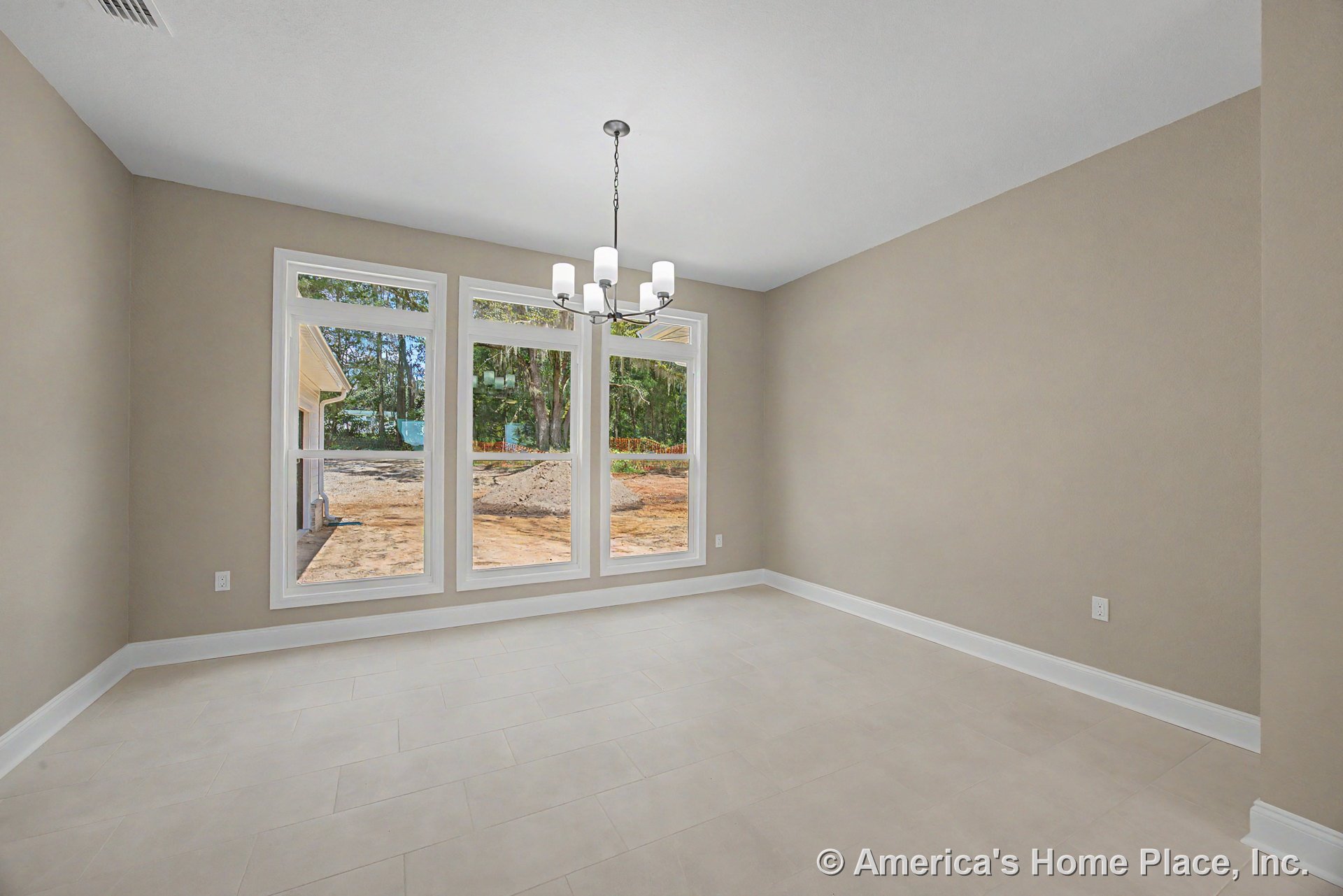 Dining area with three tall picture windows, beige tile flooring, neutral wall paint, white baseboards, modern chandelier, and rectangular room layout.