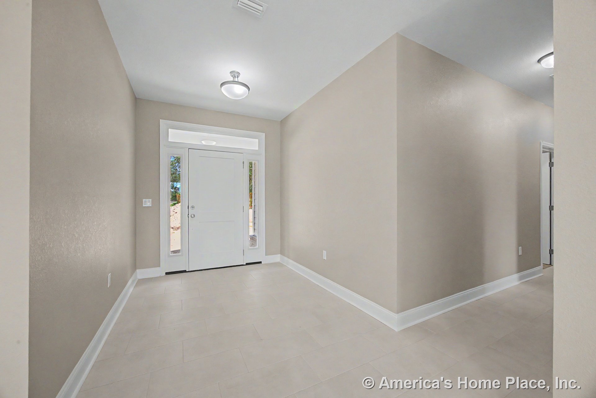 White front door with sidelights and transom window, light beige tile flooring, neutral wall paint, white baseboards, flush mount ceiling lights in foyer hallway.