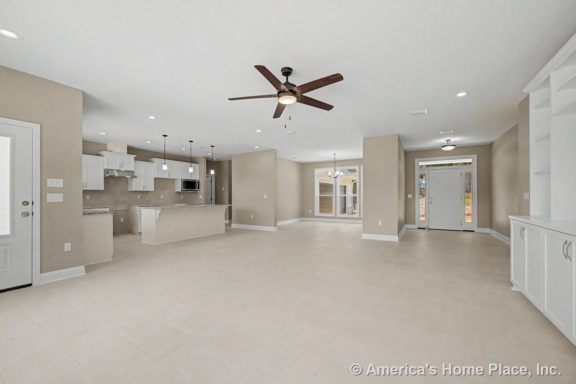 Open floor plan with tile flooring, white built-in cabinetry, kitchen island with pendant lighting, stainless steel appliances, ceiling fan in living area, recessed lighting, large