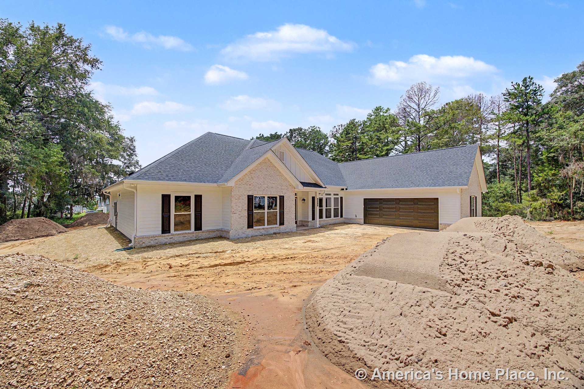 Gabled roof with brick and siding facade, covered entry porch, dark paneled two-car garage doors, multiple windows with trim, unfinished landscaping, and paved driveway.
