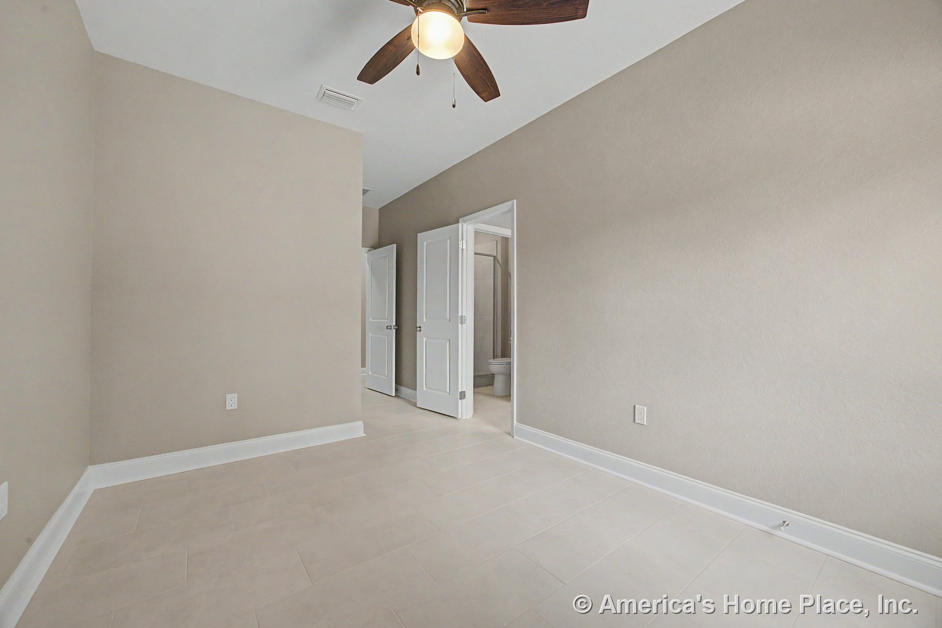 Bedroom with light tile flooring, beige walls, white baseboards and trim, ceiling fan with integrated lighting, double white doors, and entry to bathroom; modern finishes and