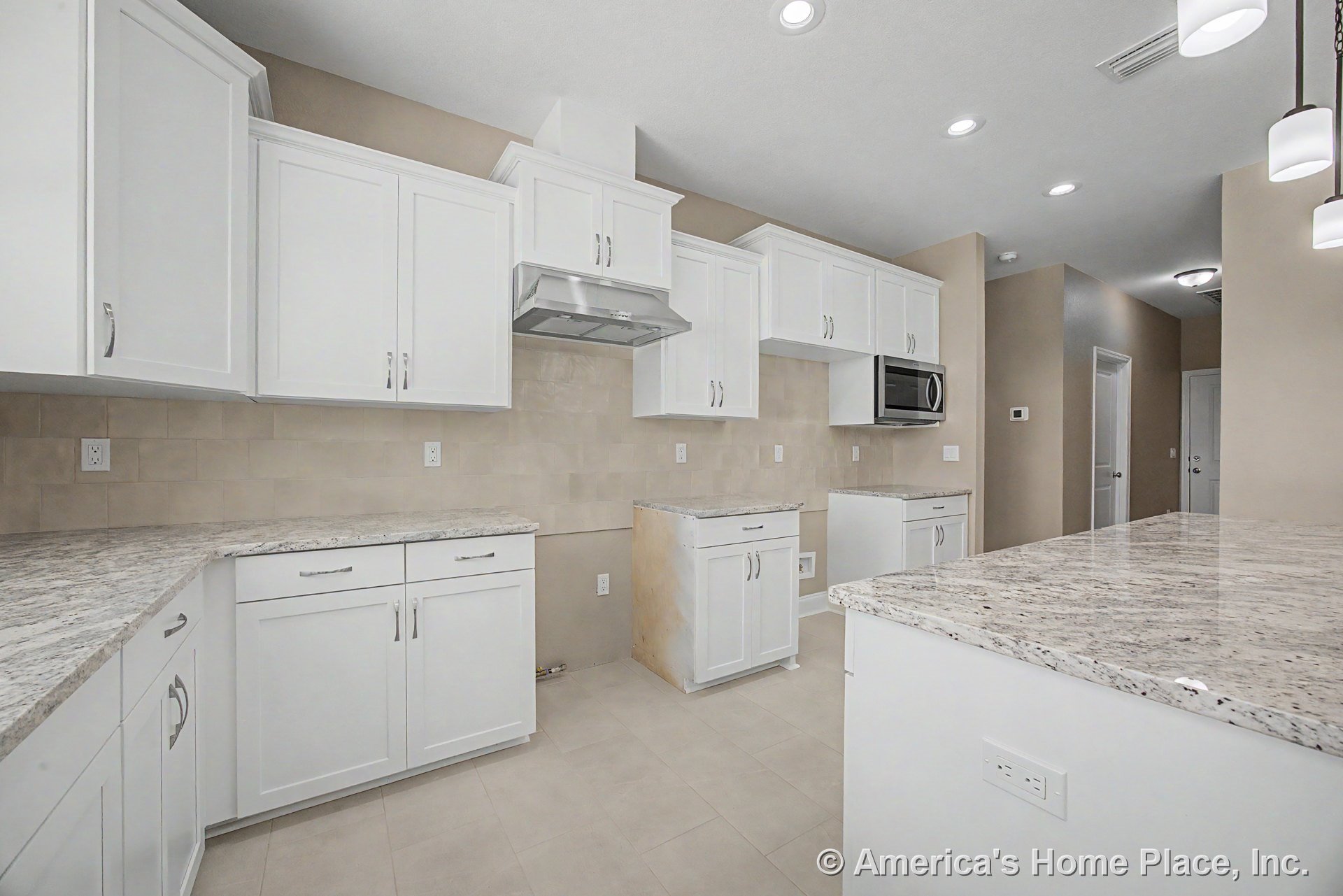 White shaker cabinets with granite countertops, tile backsplash, built-in stainless steel vent hood, mounted microwave, recessed ceiling lights, and neutral wall color above tile