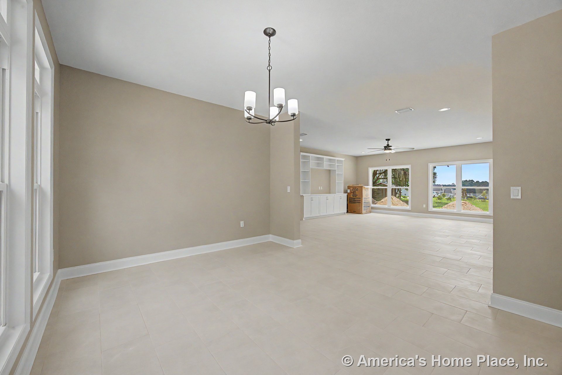 Open concept living area with built-in white cabinetry, expansive picture windows, light tile flooring, neutral wall color, recessed lighting, ceiling fan, and modern chandelier.