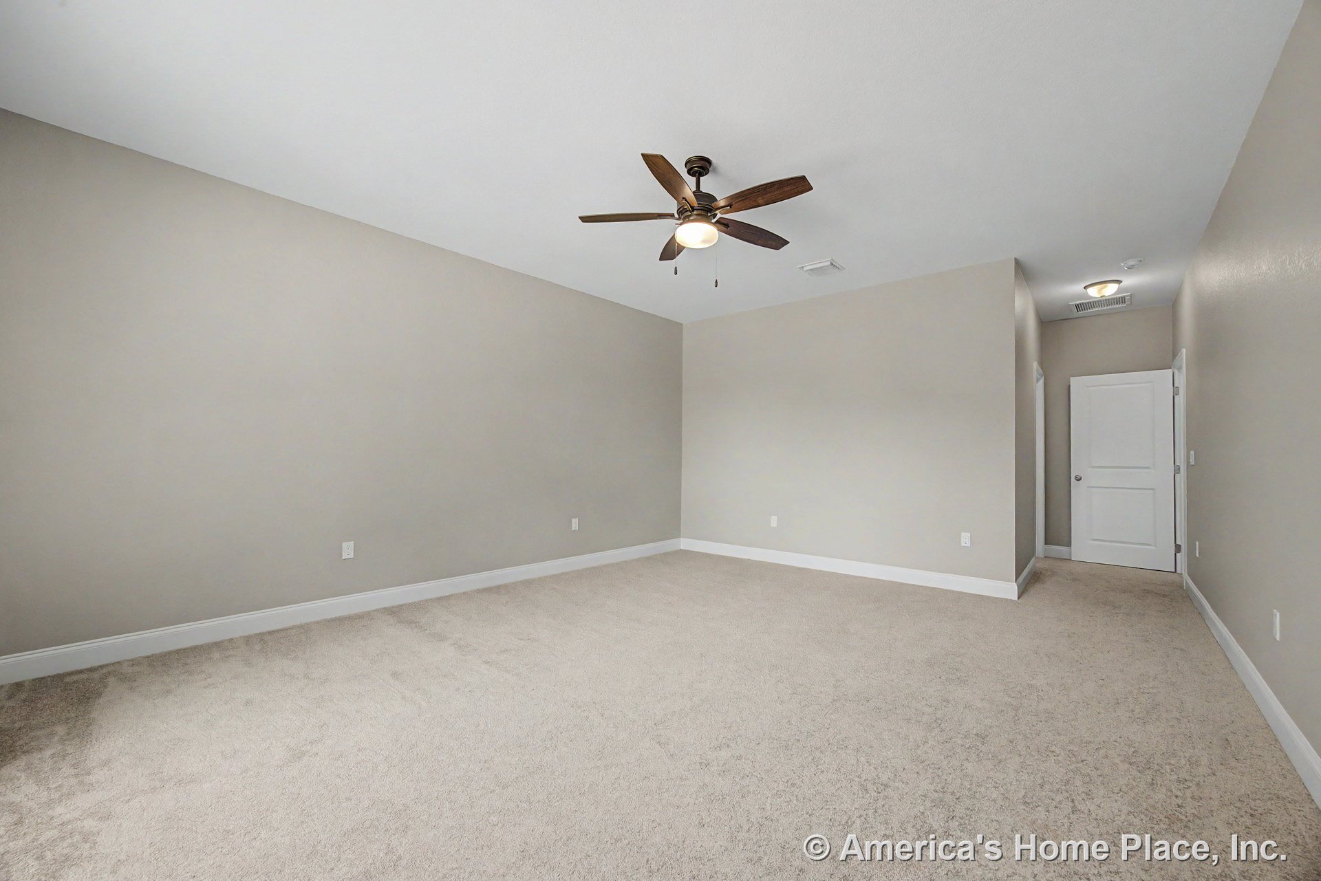 Spacious bedroom with beige carpet flooring, white baseboards, neutral wall color, ceiling fan with light, flush mount hallway light, and paneled interior door.