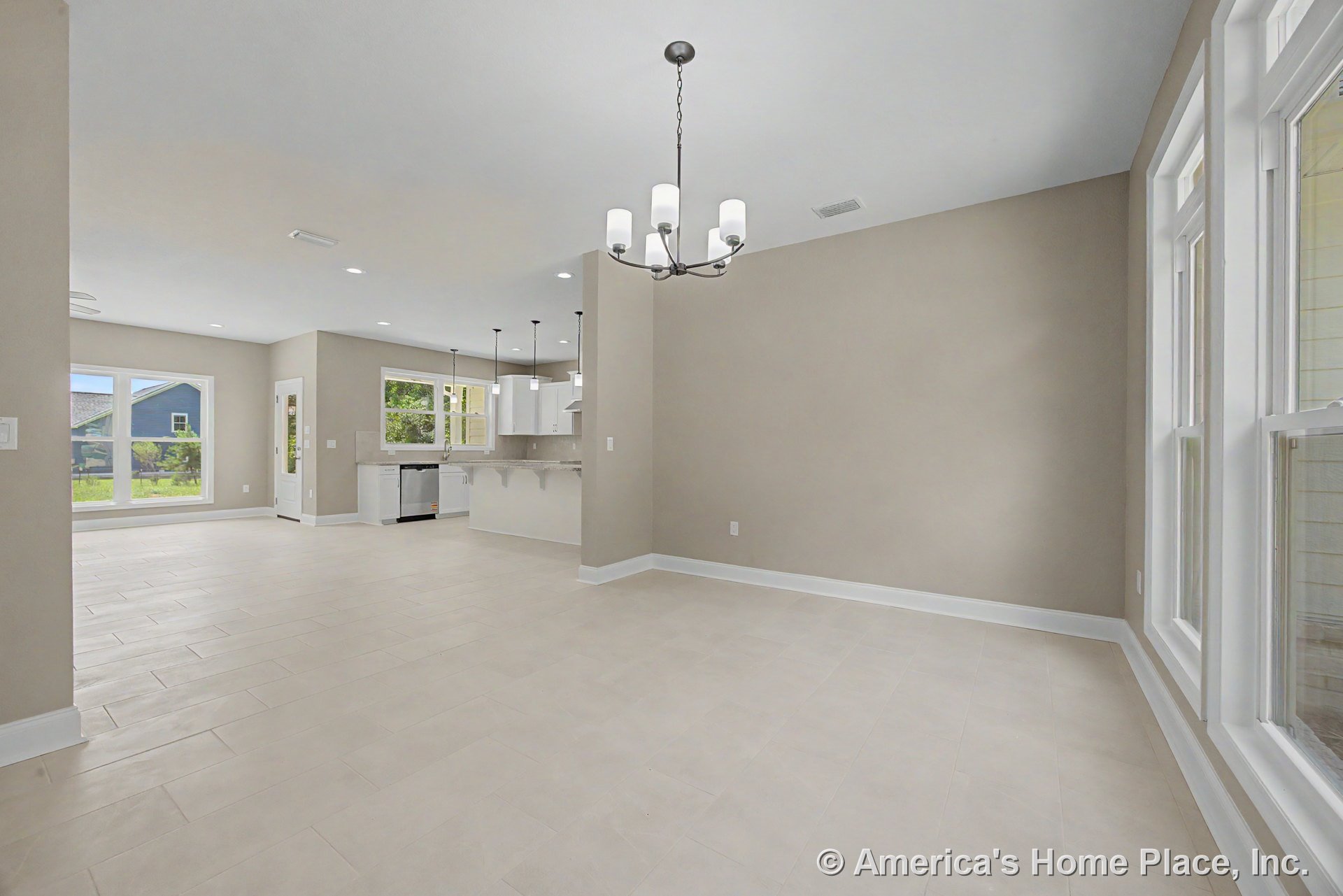 Open dining and kitchen area with large double windows, pendant lights above kitchen island, white cabinetry, granite countertops, light tile flooring, neutral walls, and recessed