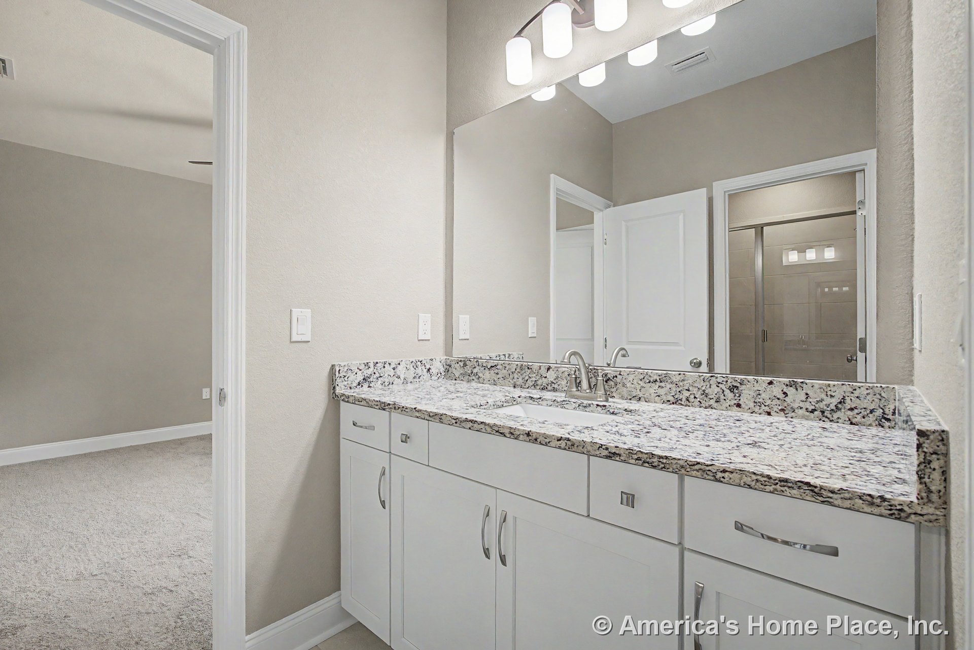 Granite vanity top with built-in sink, white shaker cabinets, large wall-mounted mirror, modern chrome faucet and light fixture, tile shower enclosure, neutral wall color, and door