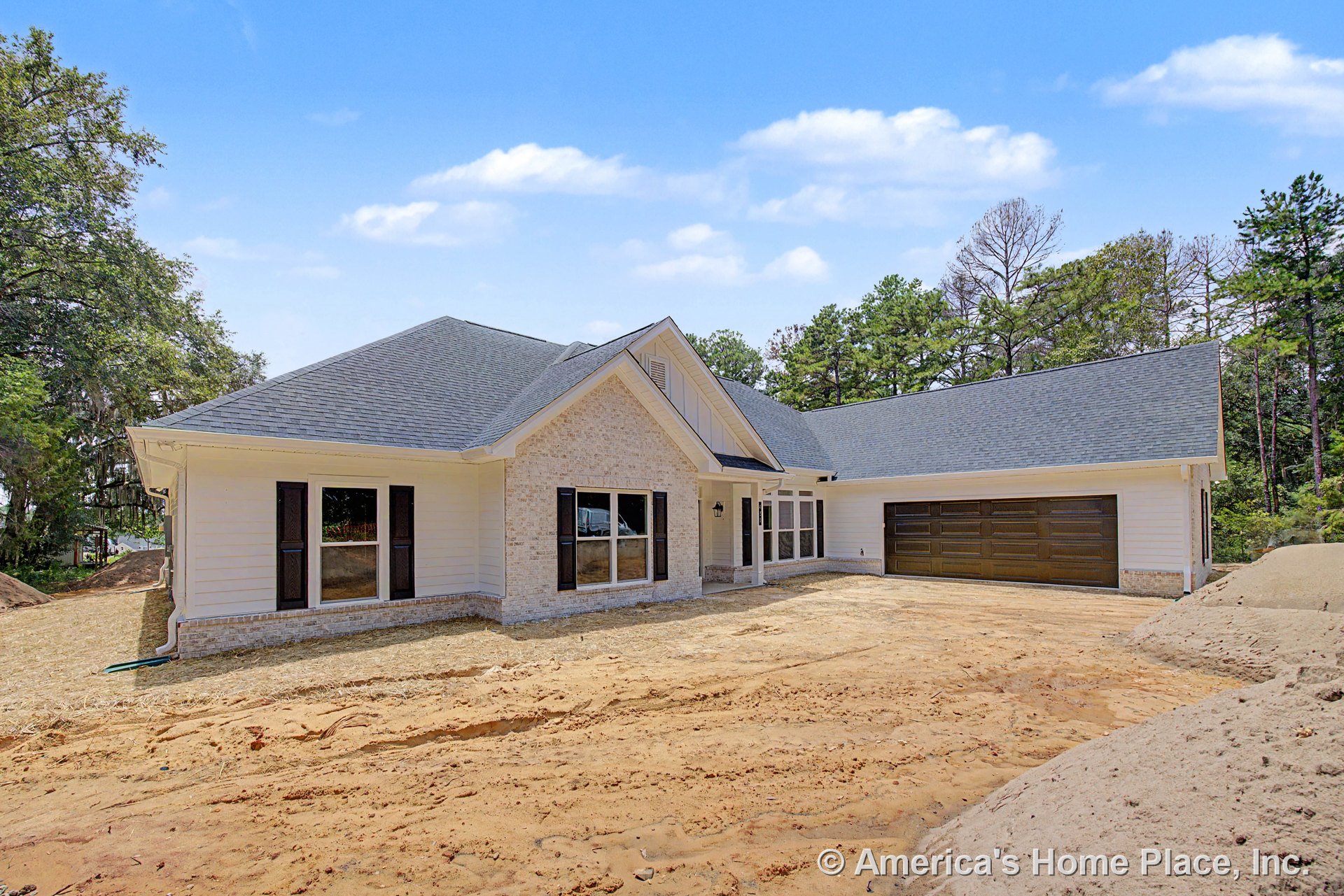 Light brick exterior with white horizontal siding, covered front porch, dark paneled two-car garage doors, black window shutters, and hip roof finished with asphalt shingles.