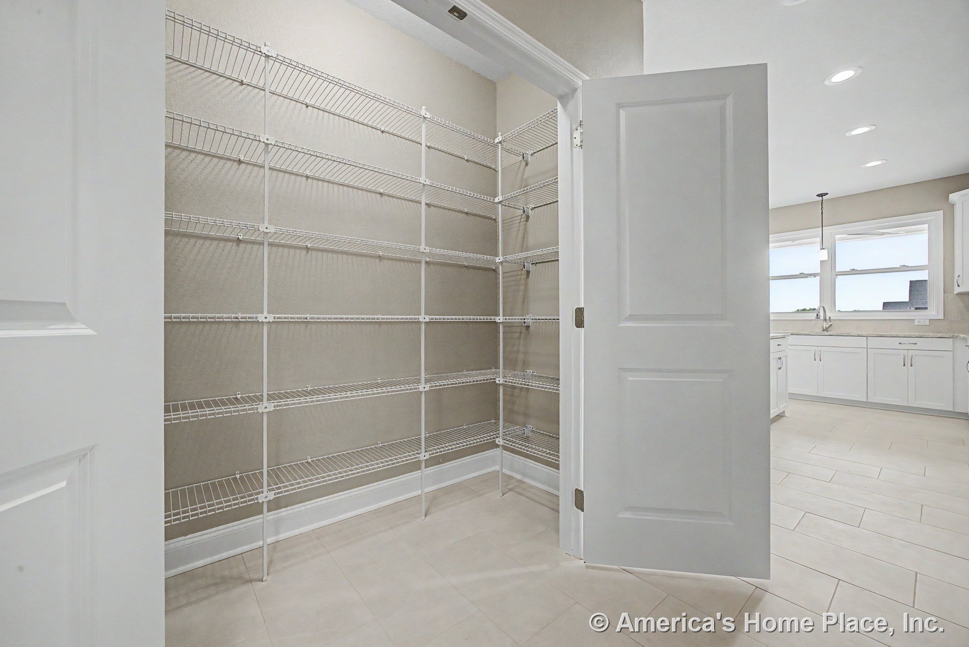 Walk-in kitchen pantry with built-in wire shelving, tile flooring, white trim, open door, adjacent kitchen cabinetry, and recessed ceiling lights.