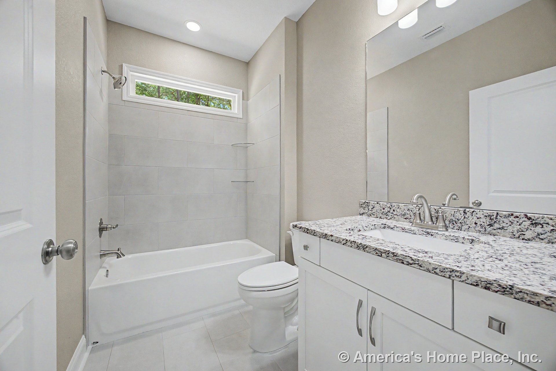 Granite vanity countertop with undermount sink, white shaker cabinets, large wall mirror, rectangular tile shower surround, horizontal transom window, recessed ceiling light, and