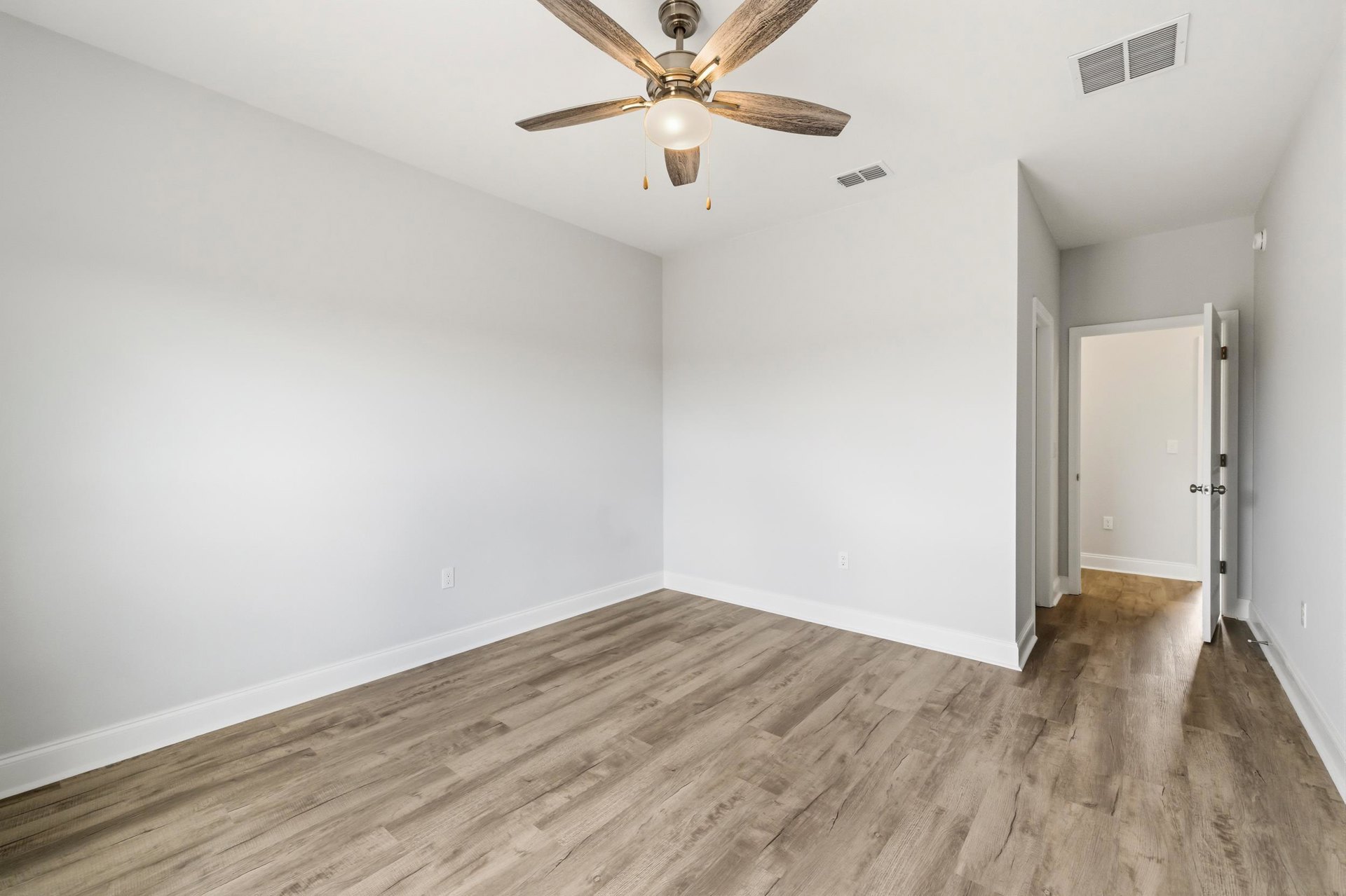 Ceiling fan with light fixture mounted above wood laminate flooring, white plaster walls, and a white door with silver knobs in a residential interior.