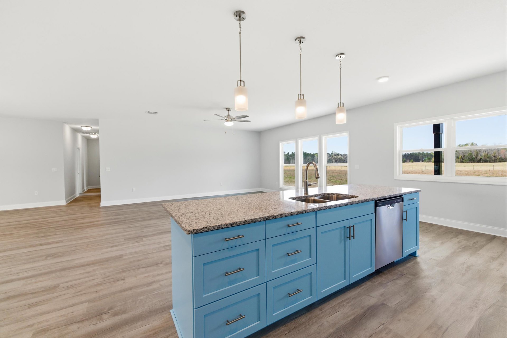 Kitchen with blue cabinets, granite countertops, large central island with built-in sink, wall-mounted light fixture, and light-colored flooring