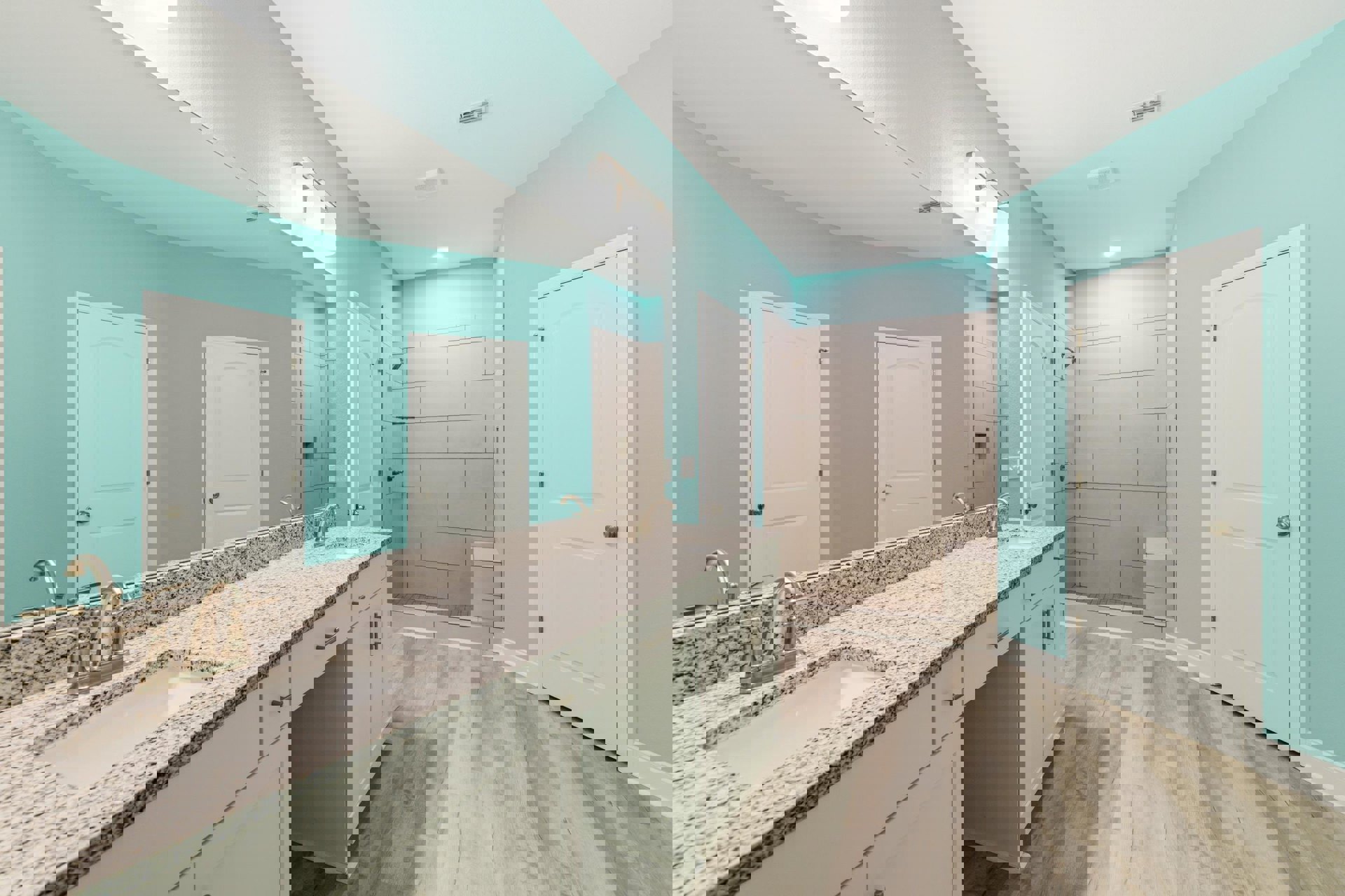 Bathroom with double sinks on granite countertop, white cabinets, blue walls, glass-enclosed shower, white door with silver handle.